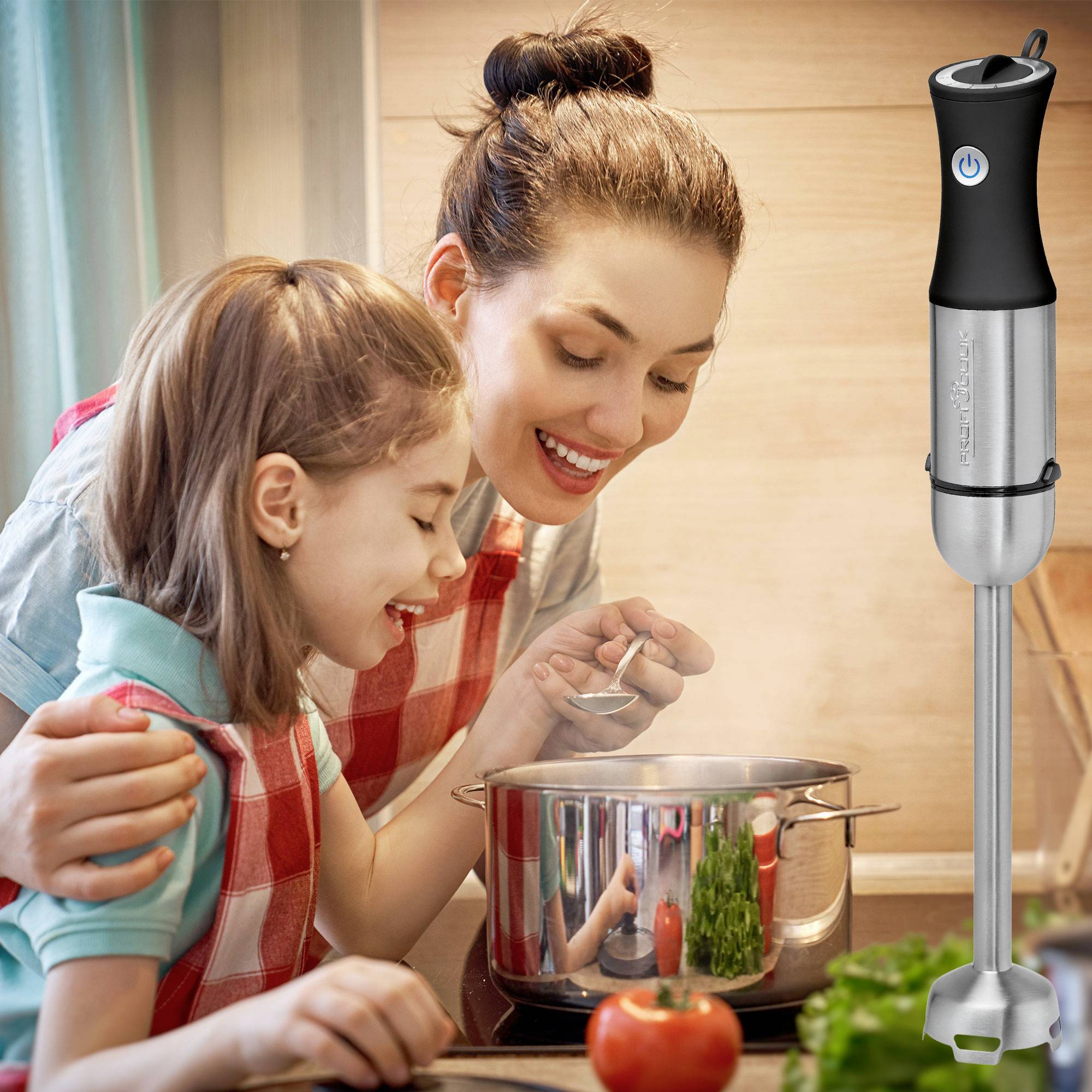 Mère et fille cuisinent ensemble dans la cuisine et regardent dans une casserole. Un mixeur plongeant est posé sur le plan de travail à leur gauche.