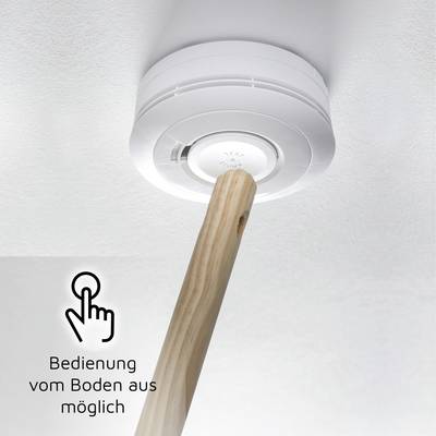 Un détecteur de fumée au plafond est actionné à l'aide d'un bâton en bois. Un symbole à côté représente un doigt et le texte indique : « Manipulation possible depuis le sol ».
