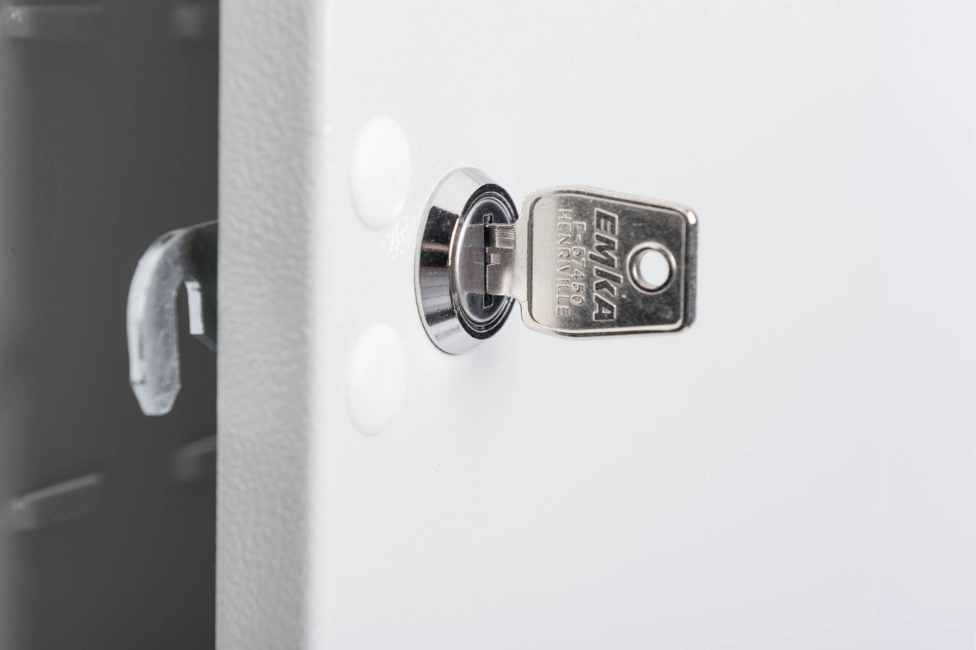 Une clé est insérée dans une serrure métallique sur une surface blanche. La serrure semble faire partie d'un grand objet ou appareil.