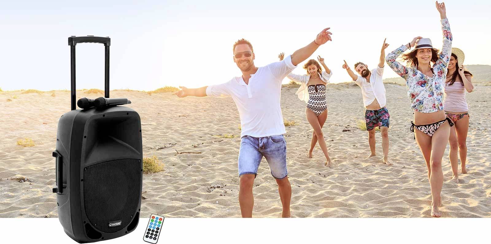 Un groupe de personnes joyeuses danse sur la plage à côté d'un grand haut-parleur avec télécommande et microphone.