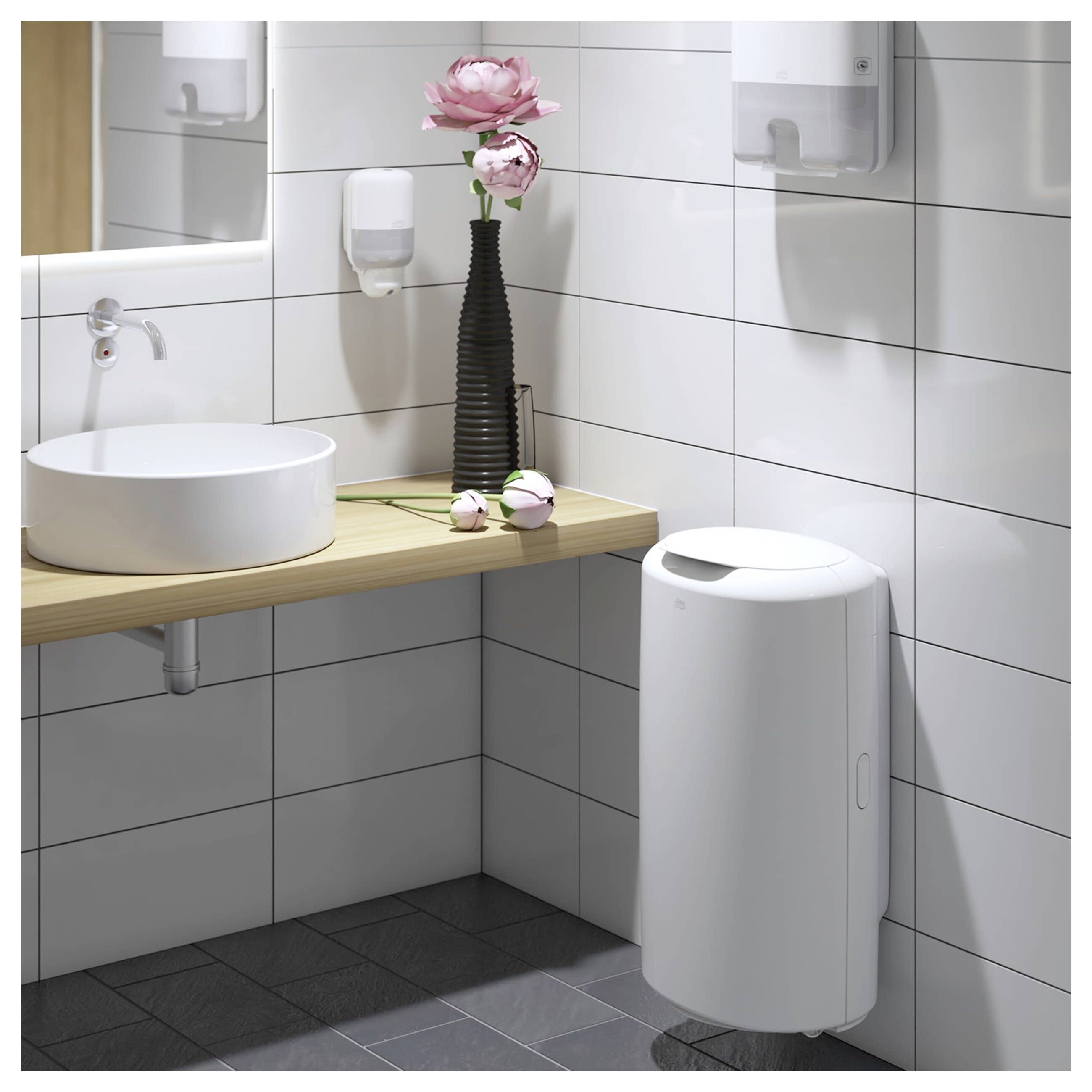 Salle de bains moderne avec lavabo blanc sur colonne, comptoir en bois, miroir mural, fleurs roses et poubelle murale.