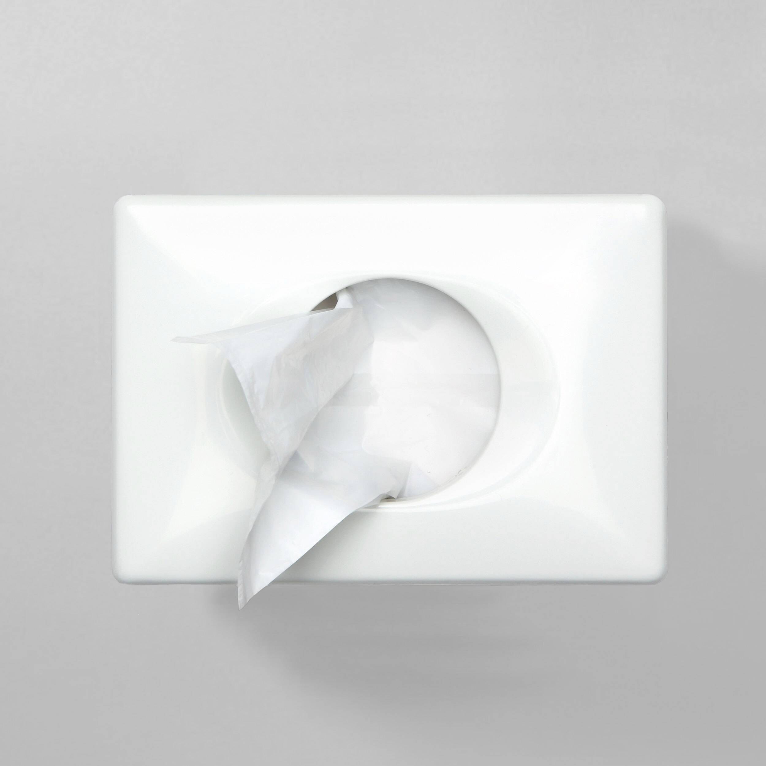 Un récipient blanc avec un mouchoir en papier qui en dépasse, sur un fond gris.