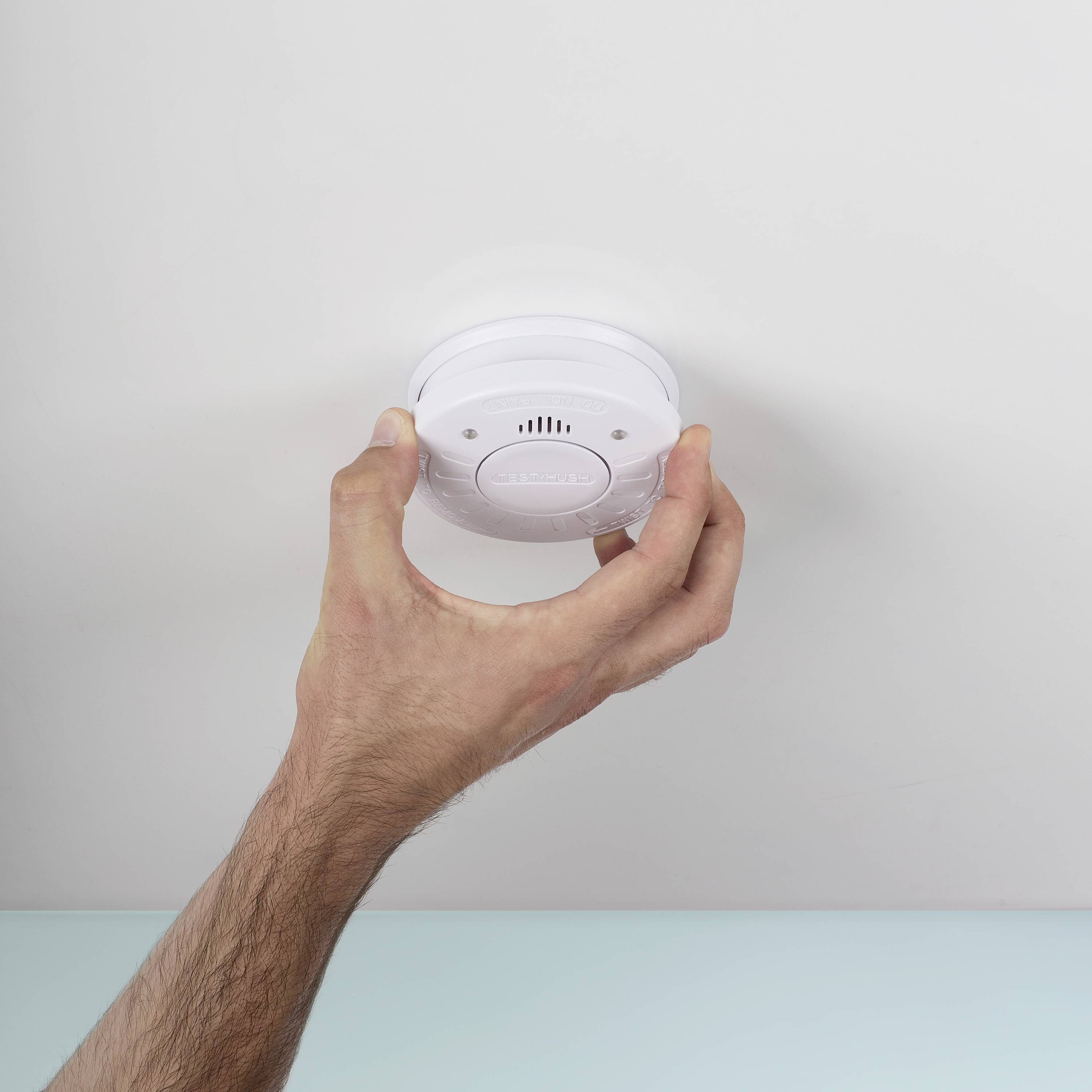 Une main installe ou teste un détecteur de fumée blanc sur un plafond.