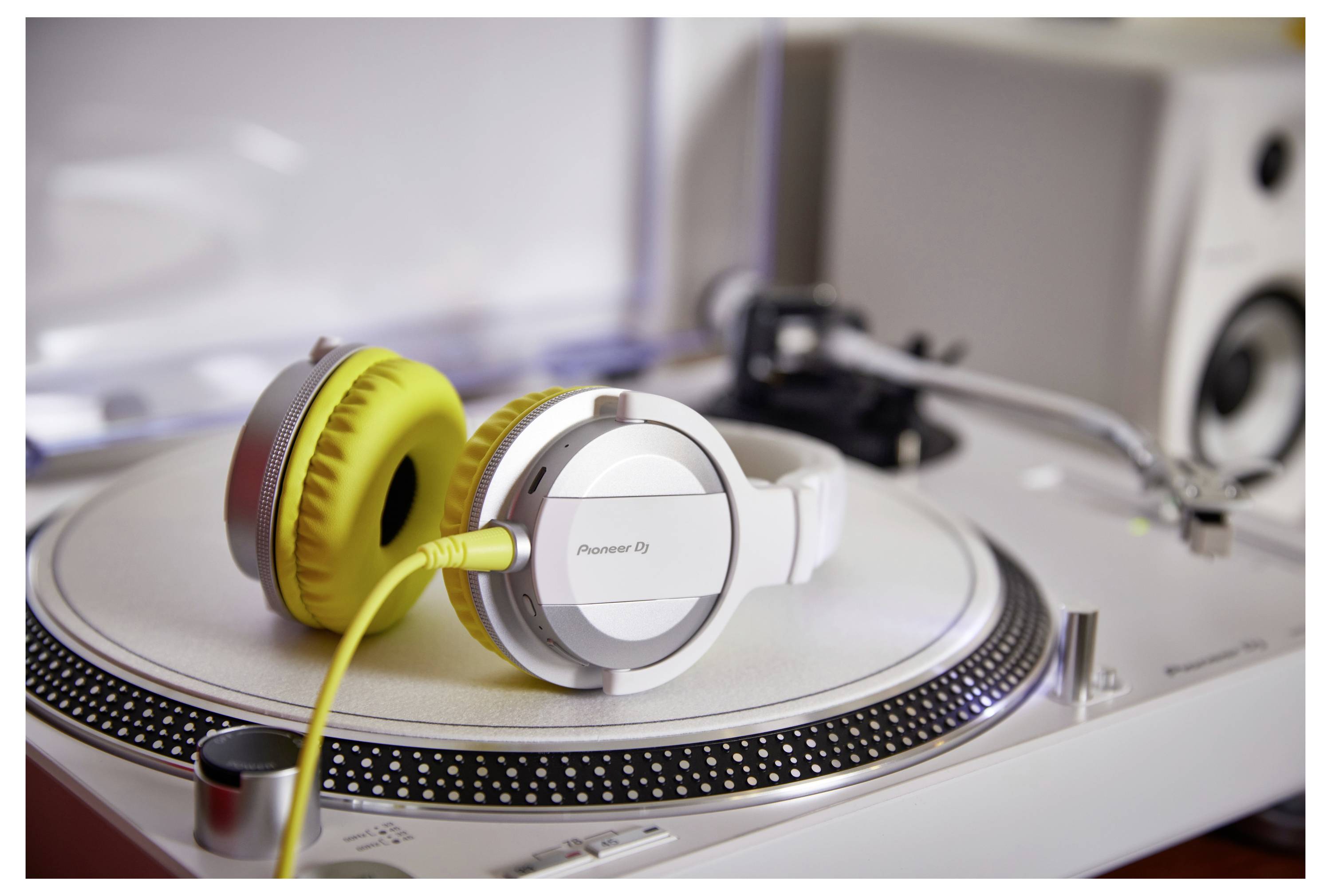 Casques DJ White Pioneer avec des coussinets auriculaires jaunes reposant sur une platine vinyle, avec un câble jaune attaché, dans une configuration musicale.