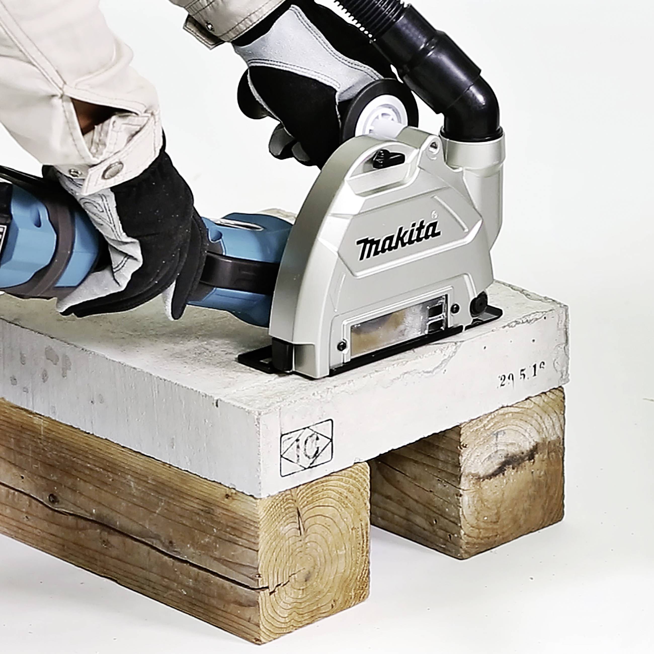 Une personne utilise un outil électrique pour poncer une surface en béton, avec du bois servant de support.