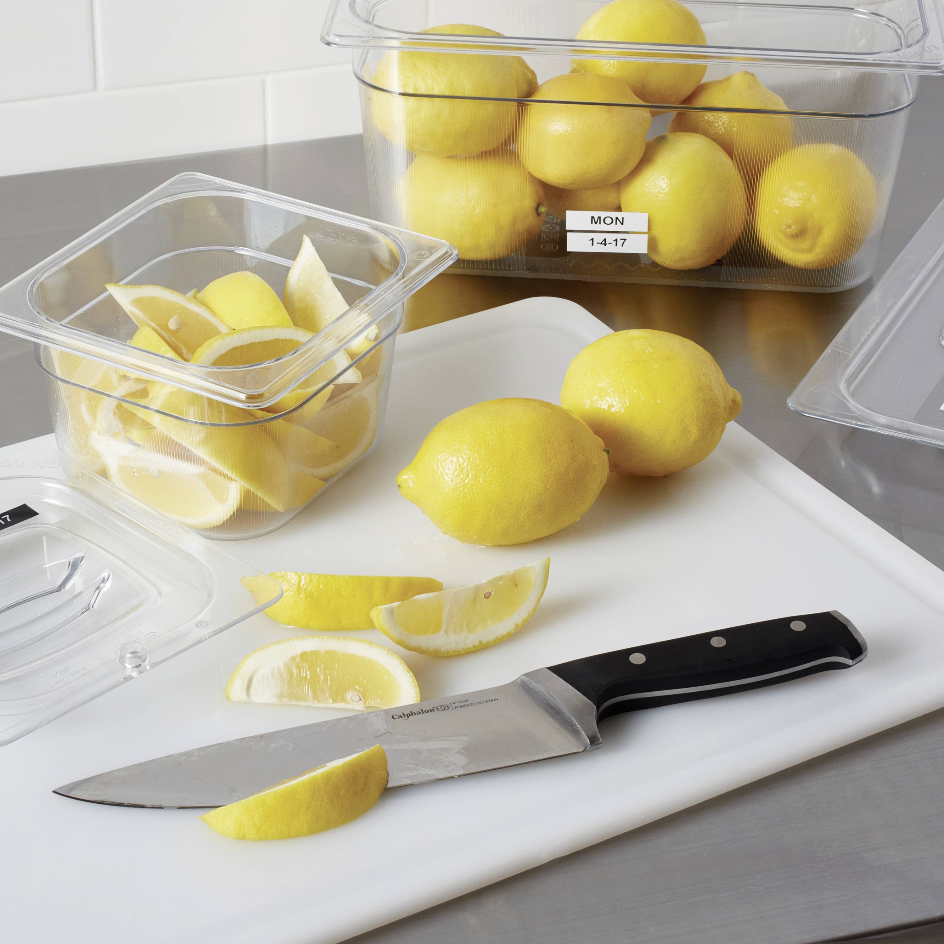 Plusieurs citrons sur une table, dont certains sont coupés dans un récipient ouvert. Un couteau est posé à côté d'une planche à découper avec des tranches de citron.