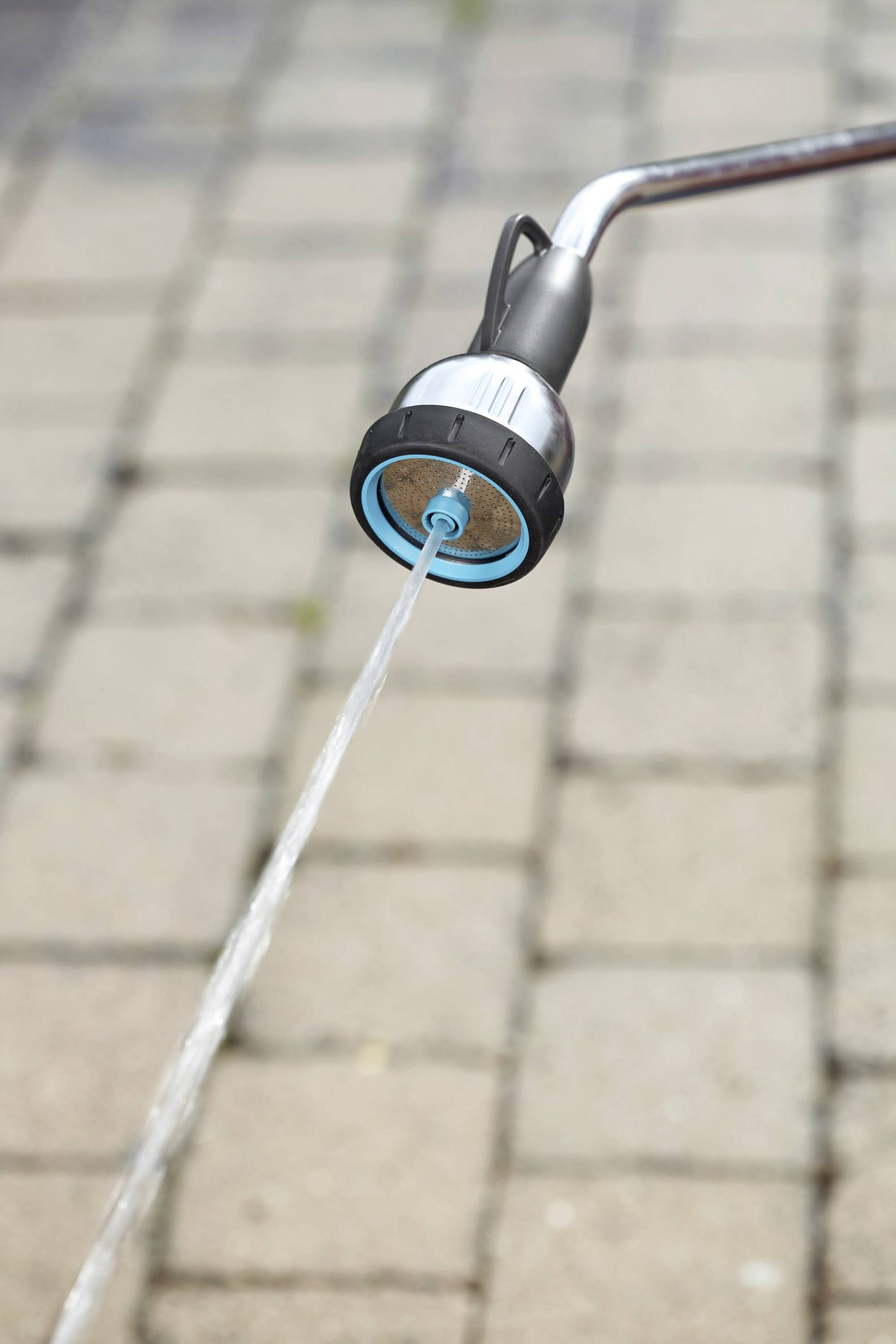 Un tuyau d'arrosage projette un jet d'eau sur une surface pavée.