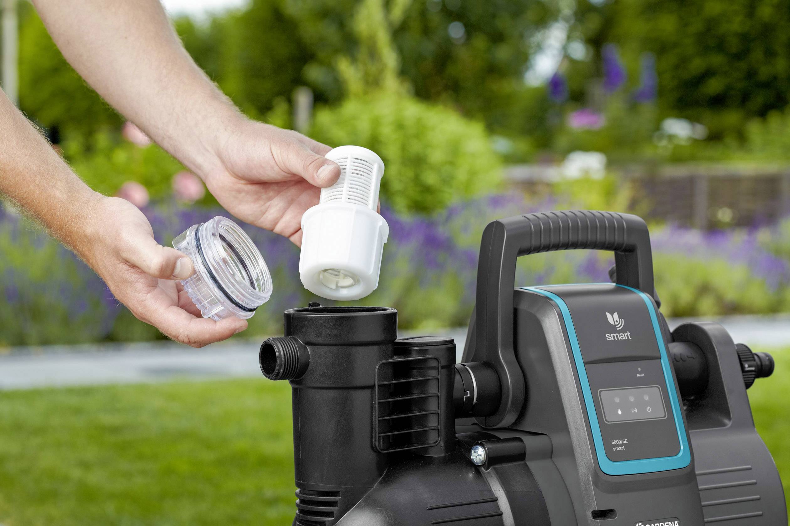 Une personne installe un filtre dans une pompe à eau de jardin. L'environnement est un jardin bien entretenu.