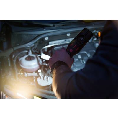 Une personne tient un appareil de diagnostic au-dessus d'un compartiment moteur ouvert afin d'analyser ou de réparer des problèmes techniques.