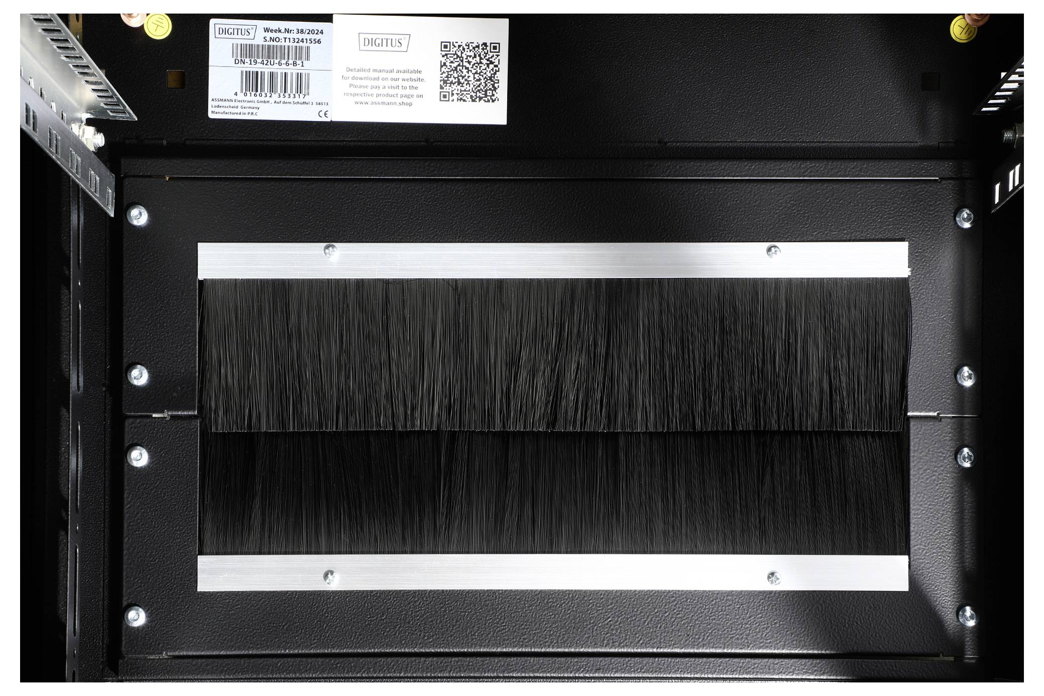 Un boîtier métallique noir avec une barre de brosses à câbles à l'intérieur. Il dispose d'une plaque signalétique et d'un code QR sur le dessus. Des vis sont visibles sur les côtés.