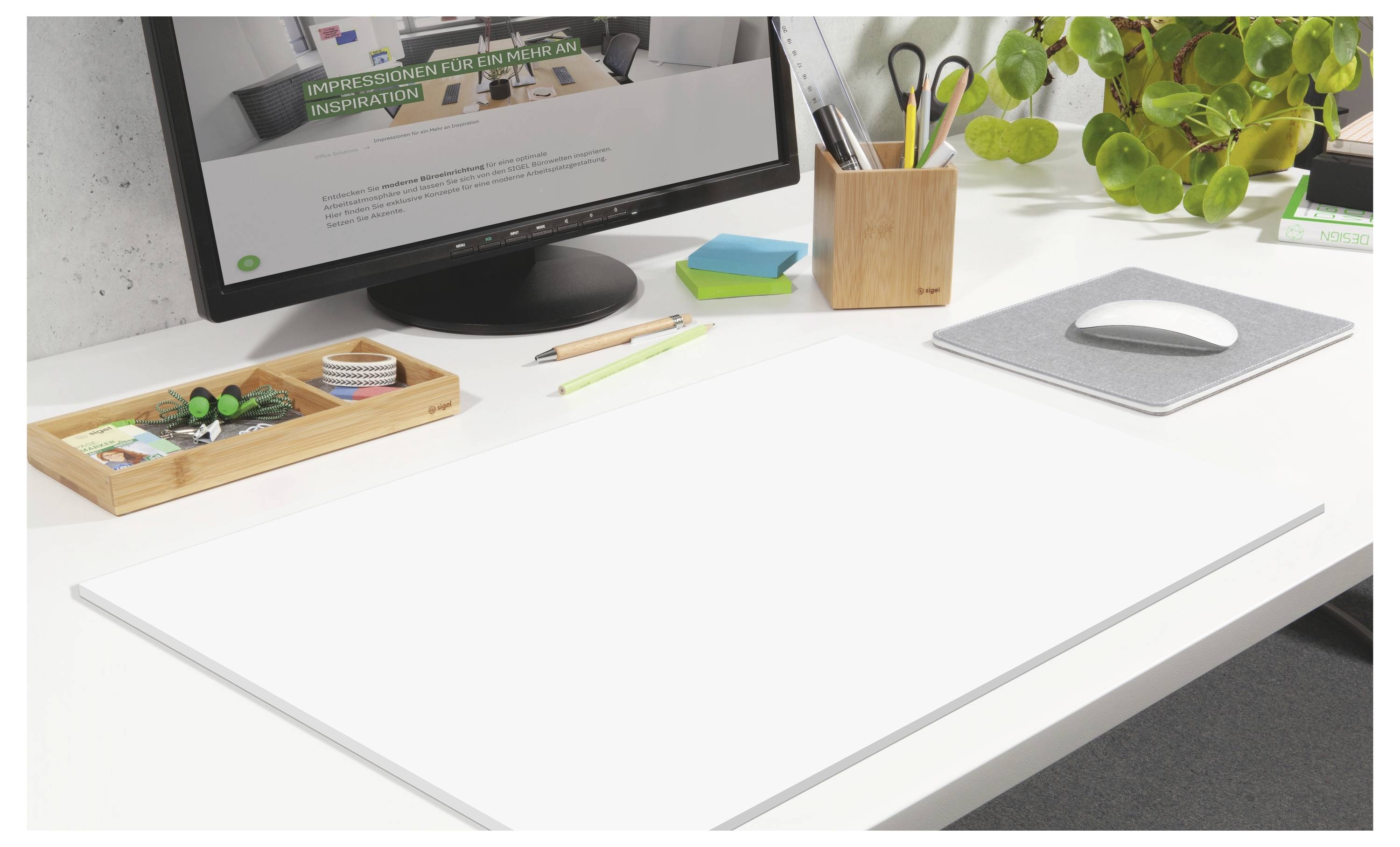 Bureau blanc minimaliste avec moniteur, porte-stylos, plateau de fournitures, tapis de souris et petite plante dans un espace de travail bien organisé.