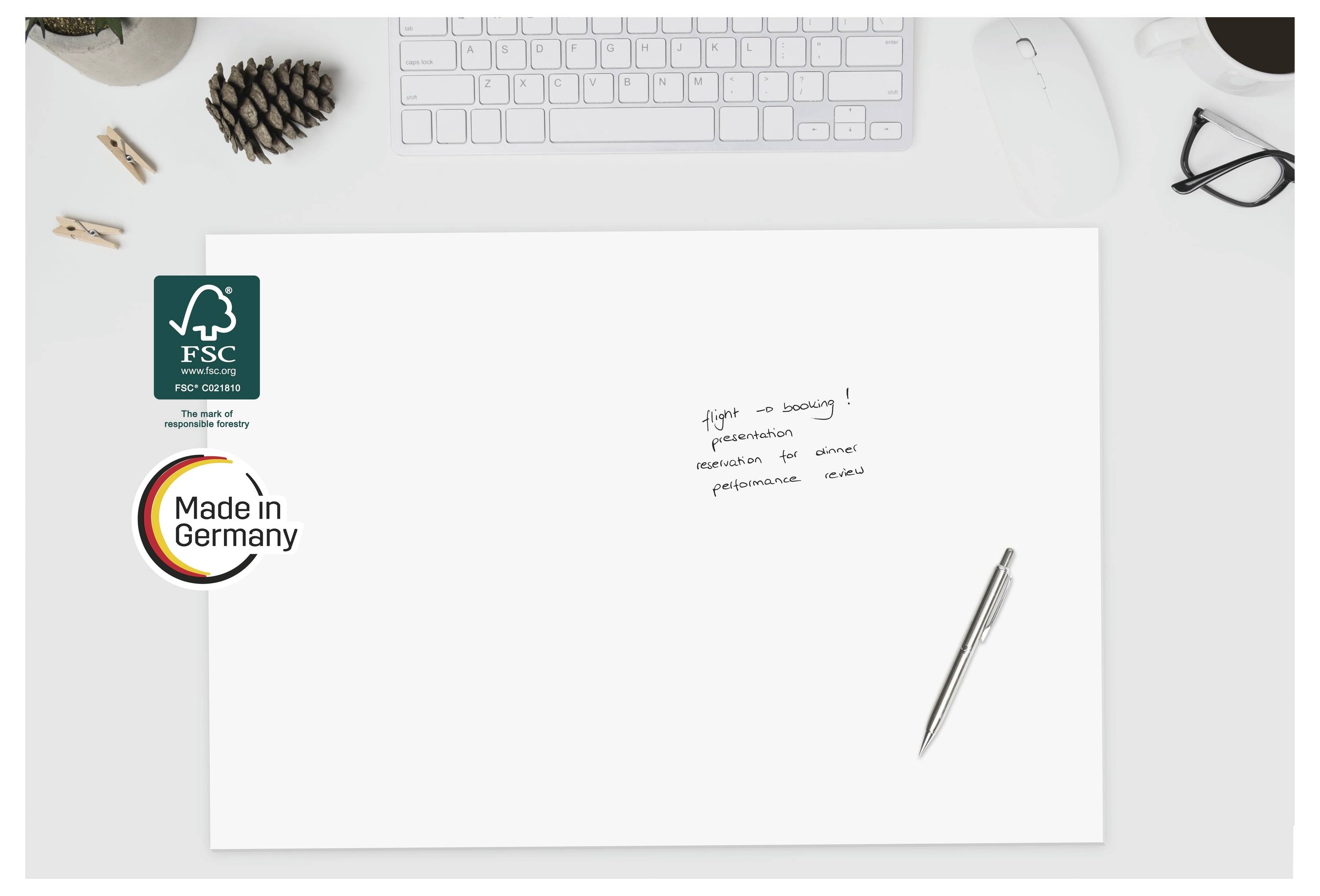 Feuille blanche vierge sur un bureau avec les logos FSC et Fabriqué en Allemagne, un stylo, un clavier, des lunettes et de petites notes manuscrites sur la page.