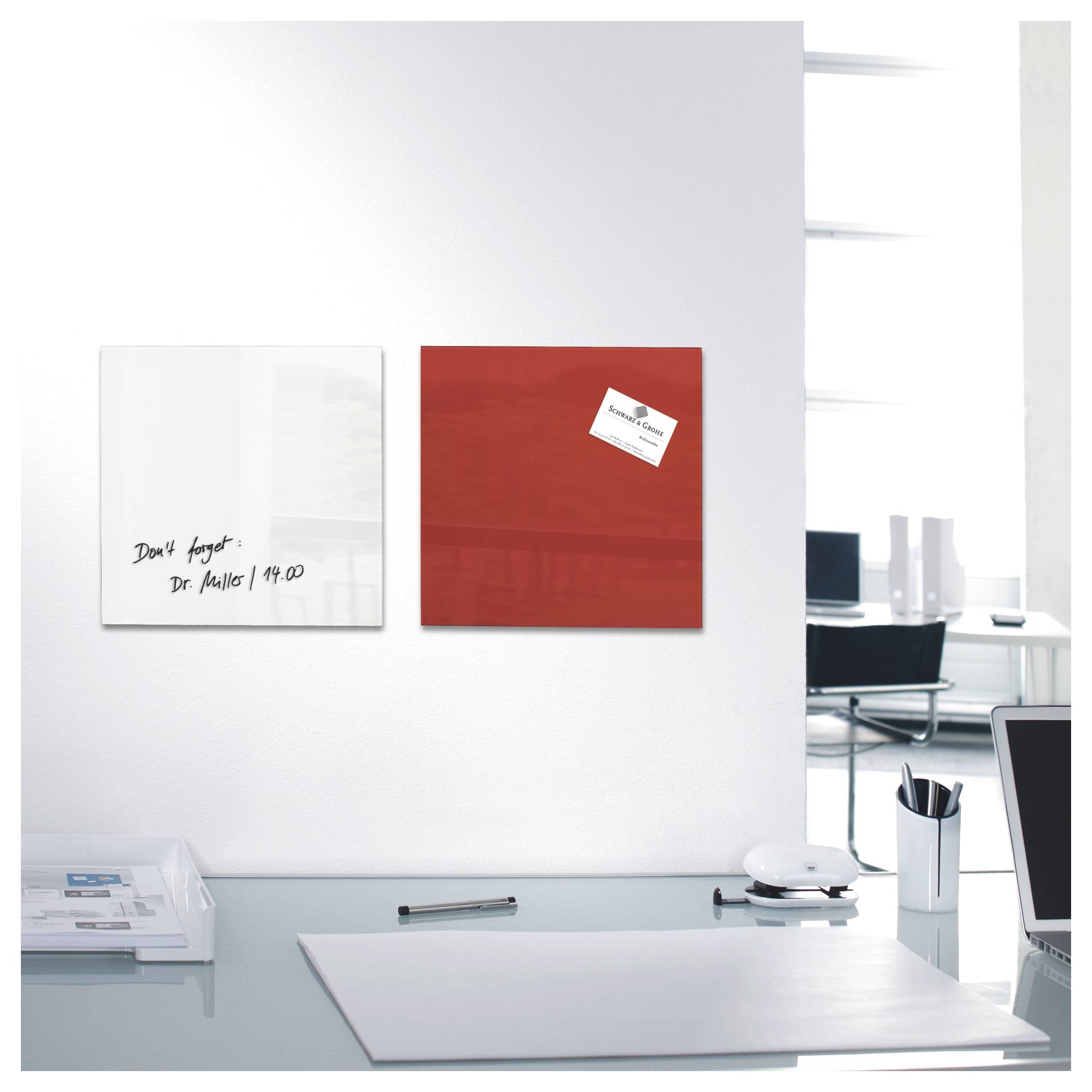 Bureau de bureau moderne avec deux tableaux carrés montés au mur, l'un blanc avec une note manuscrite et l'autre rouge avec une petite carte de visite