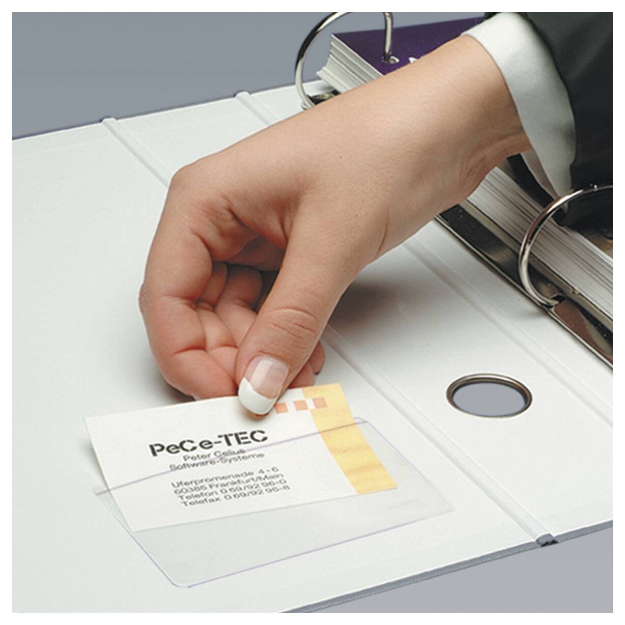 Une main plaçant une carte de visite dans une pochette transparente d'un classeur à anneaux, suggérant l'organisation des documents ou le classement.