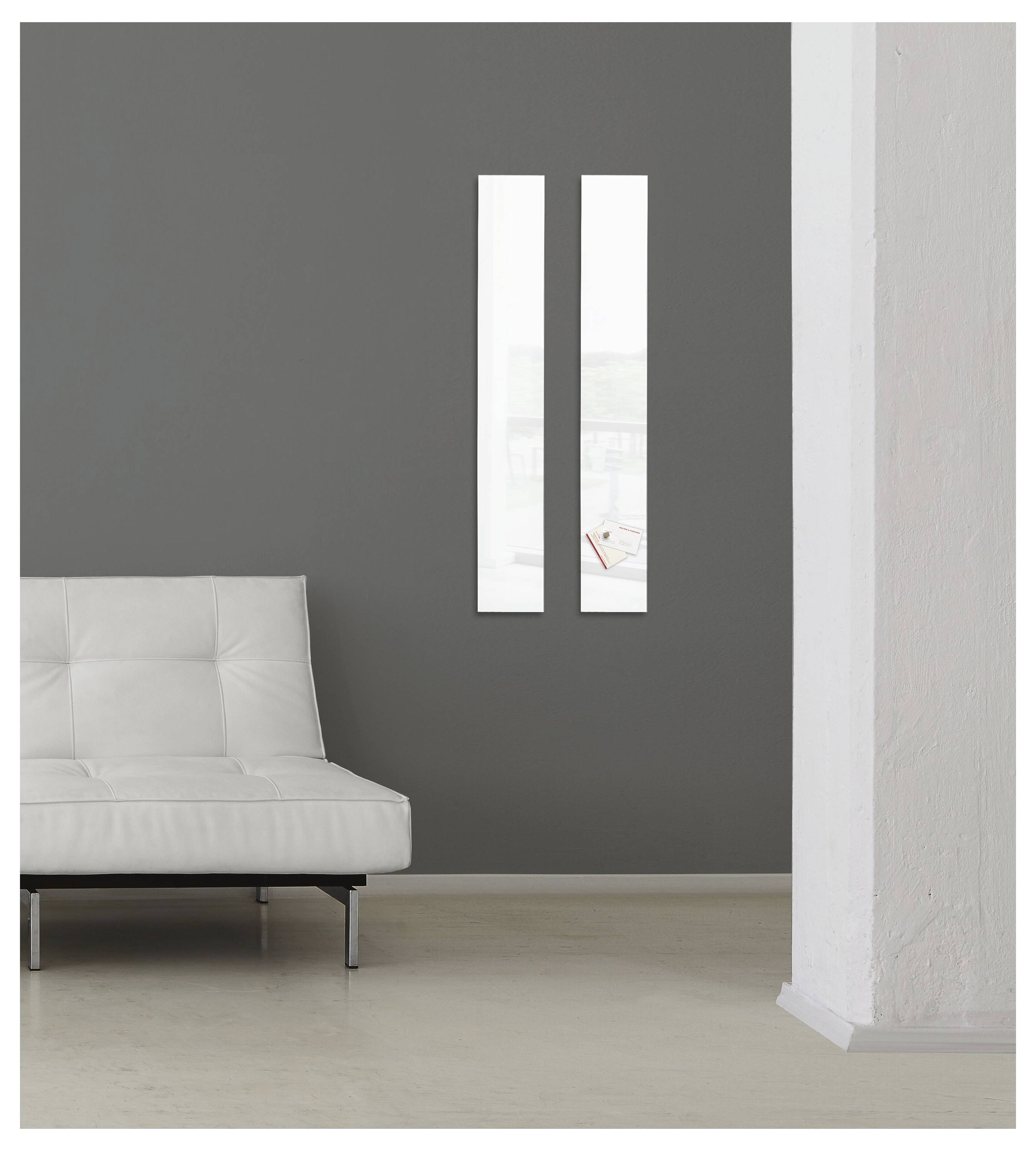 Intérieur minimaliste avec un canapé blanc contre un mur gris foncé, deux fenêtres verticales étroites, et une colonne blanche sur la droite.