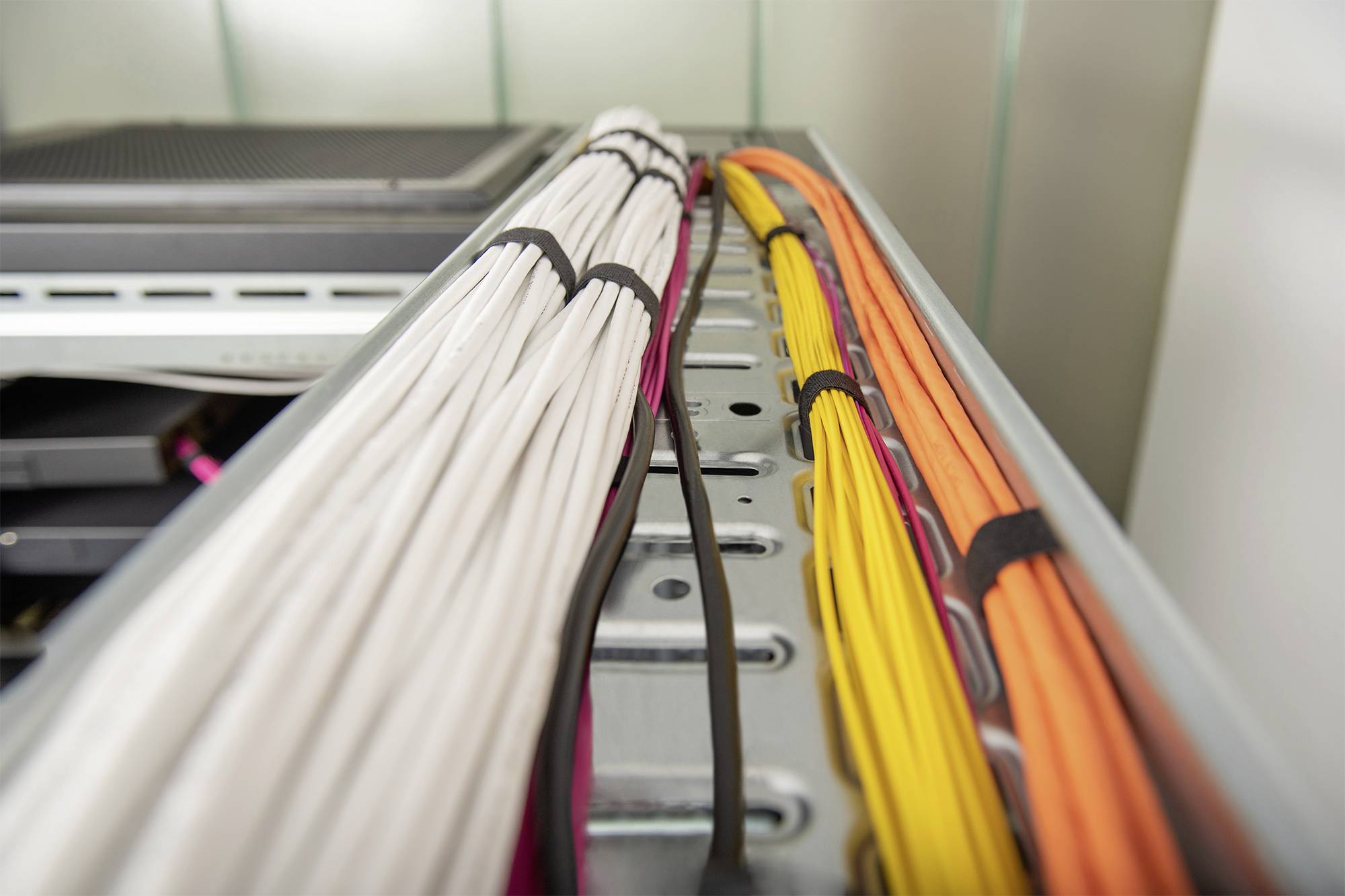 Un faisceau de câbles blancs, oranges et jaunes, soigneusement fixés sur un rack de serveur, symbolise une infrastructure informatique bien organisée.