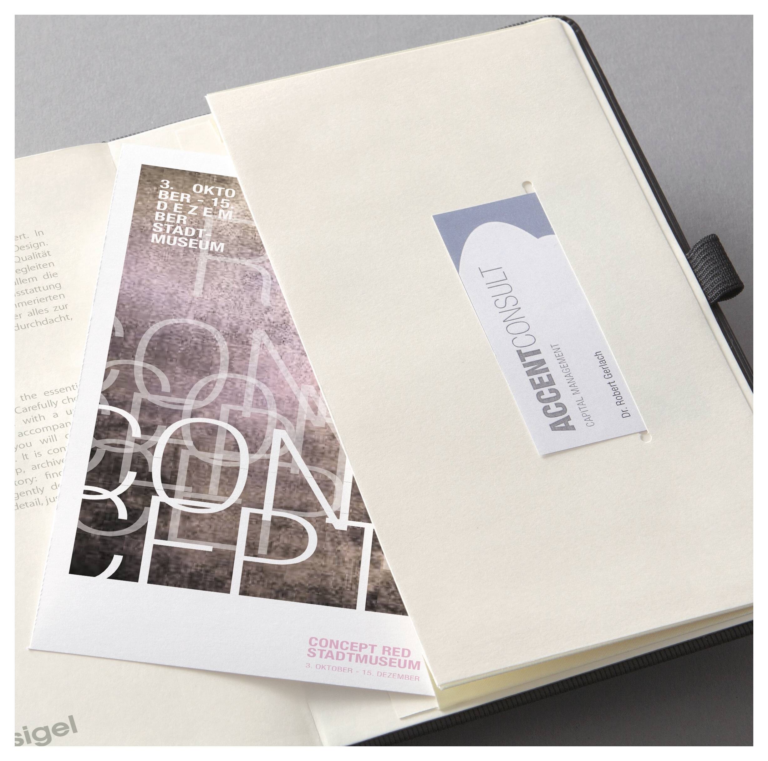 Un cahier crème repose sur un catalogue d'art et des papiers, avec une étiquette verticale « ACCENT CONSULT » sur la couverture.