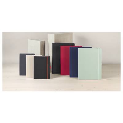Carnets reliés assortis aux couleurs sourdes disposés sur une surface en bois clair, plusieurs se dressant verticalement et se chevauchant.