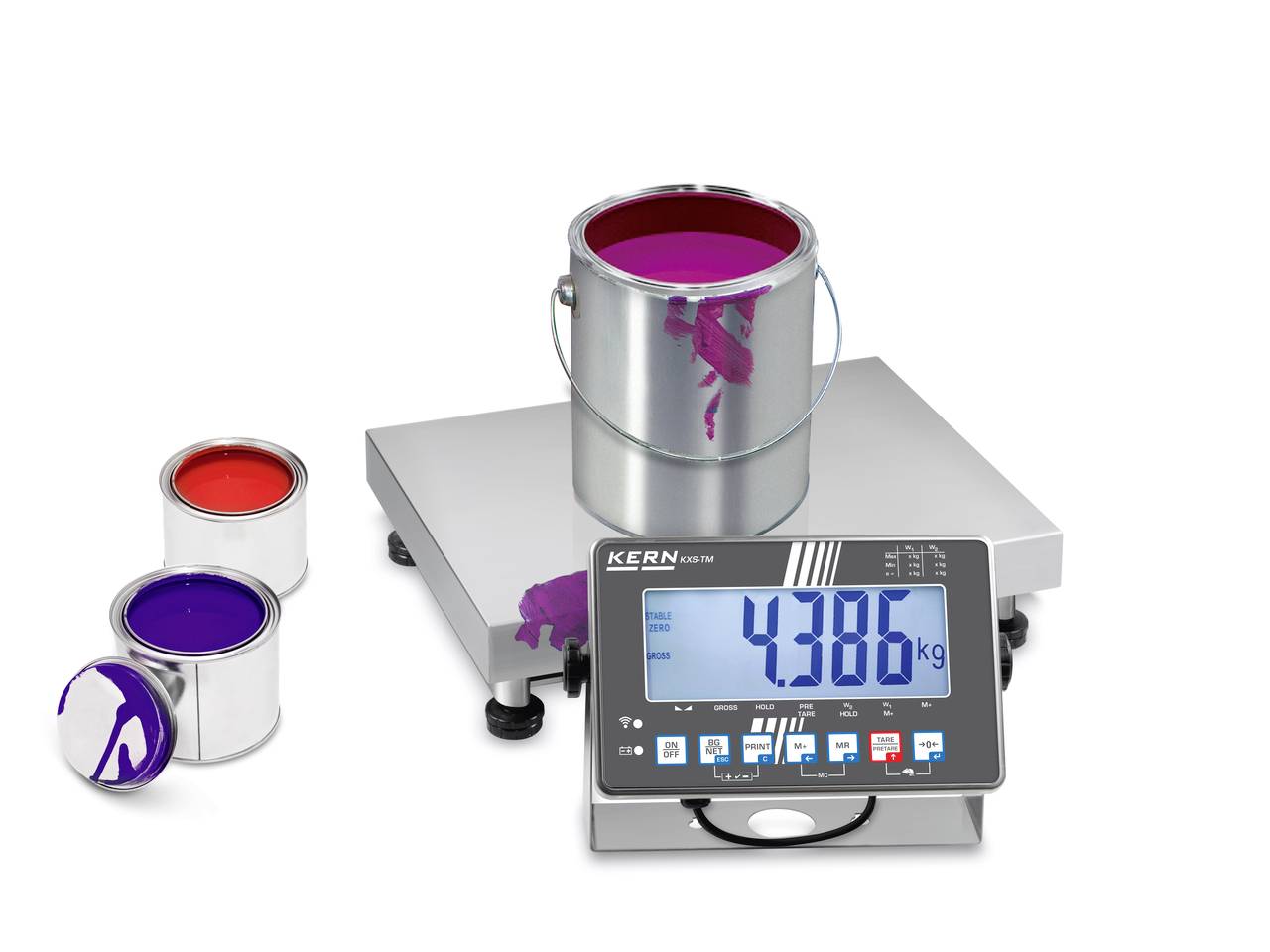 Une balance affiche un poids de 4,386 kg. Sur cette balance se trouve un seau de peinture ouvert de couleur lilas. À côté, deux autres boîtes de peinture sont posées.