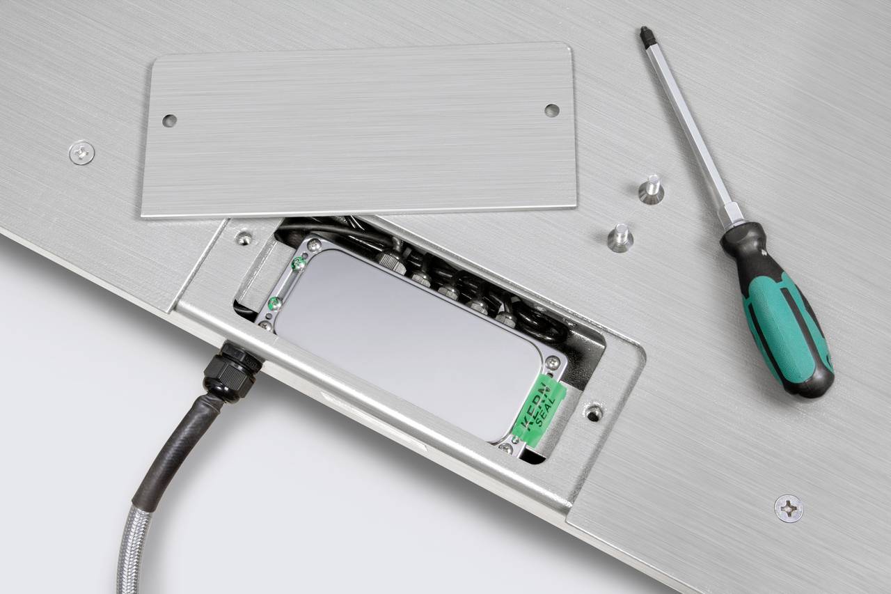 Un canal de câbles ouvert avec des câbles visibles et un tournevis à côté. Une plaque de couverture est partiellement retirée.