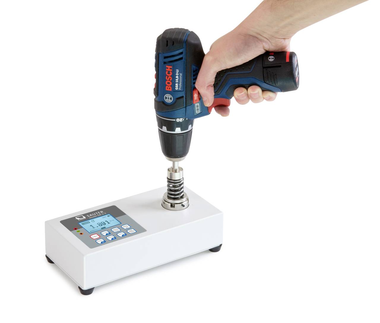 Une main tient une visseuse-perceuse fixée à un appareil de mesure blanc en position verticale.