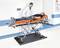 Un médecin examine un patient sur un brancard orange posé sur une balance, dans une salle médicale.