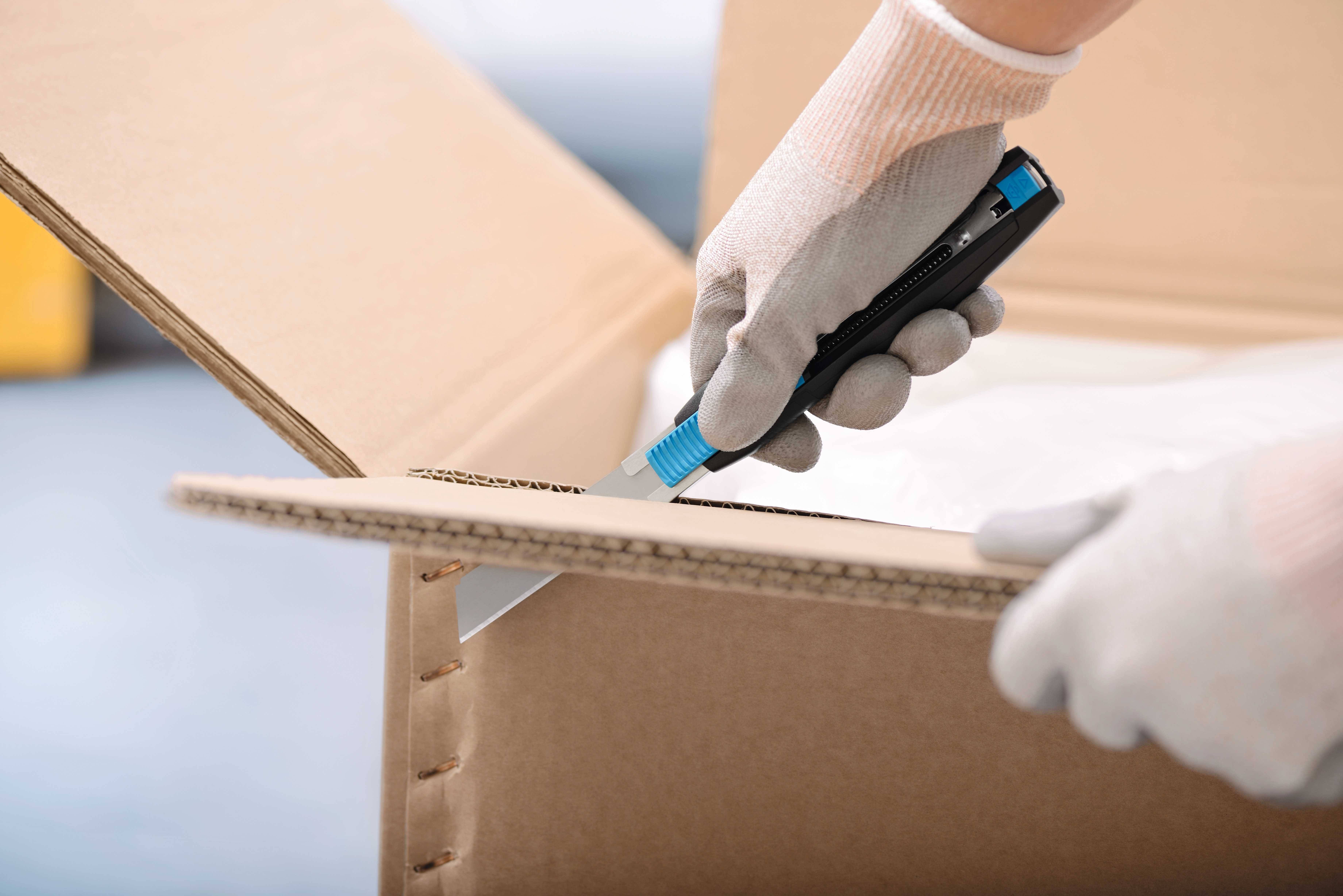 Une personne portant des gants ouvre un carton en utilisant un cutter.