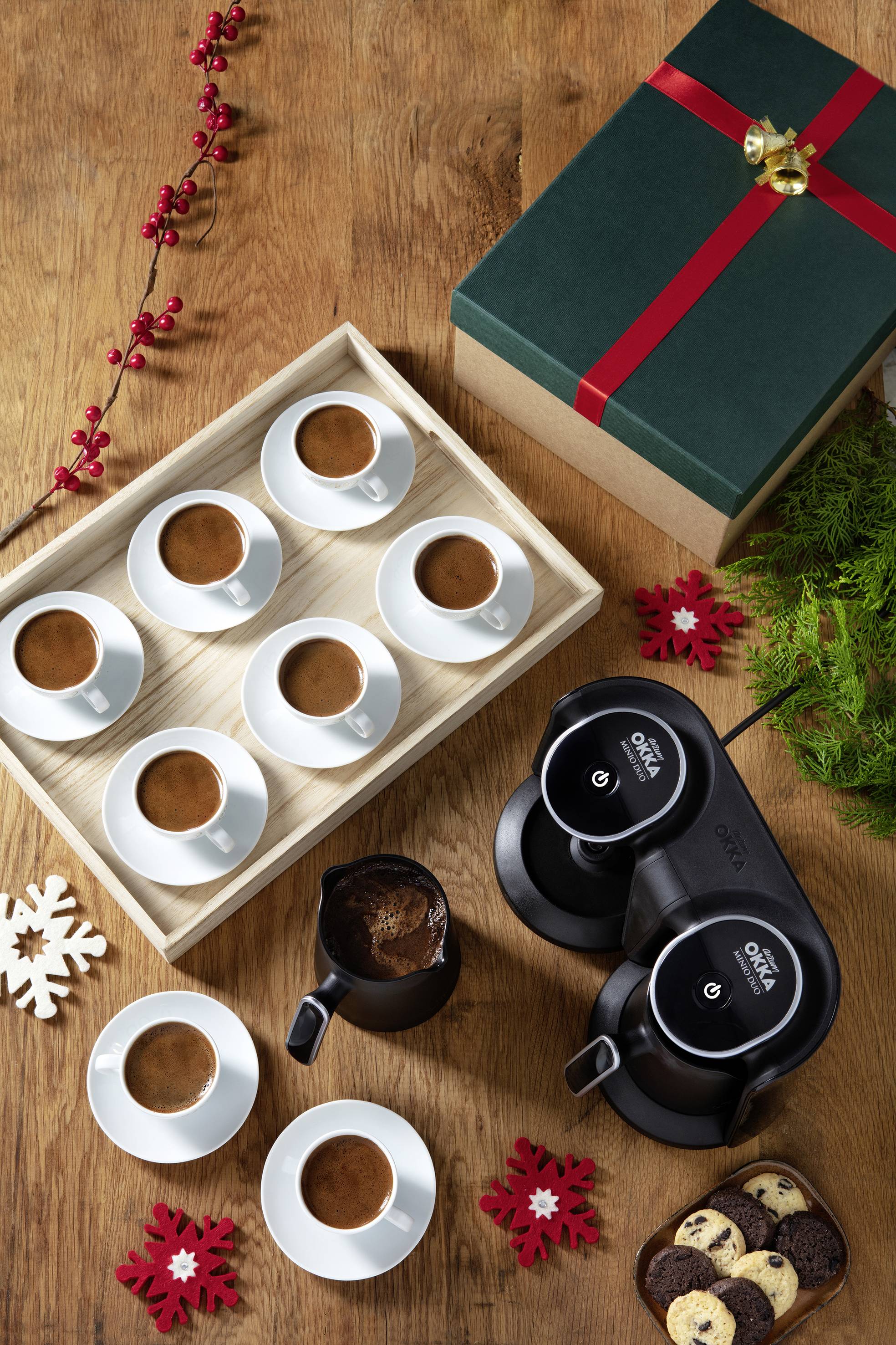 Machine à café avec plusieurs tasses de café frais sur une table en bois à côté d'un paquet cadeau vert et de décorations de Noël.