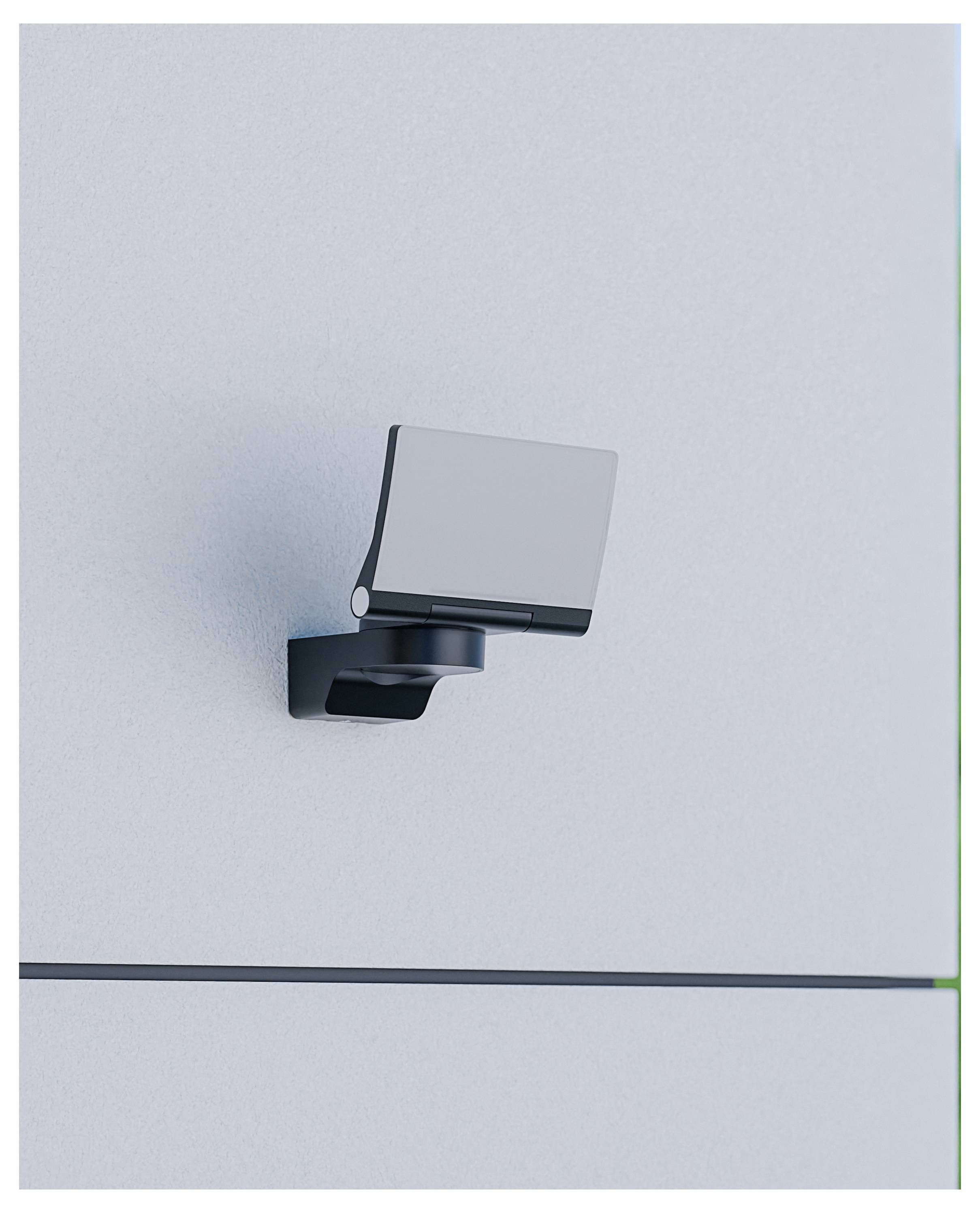 Petit levier ou poignée noir fixé au mur sur un panneau métallique gris clair, avec une couture horizontale dans la partie inférieure.