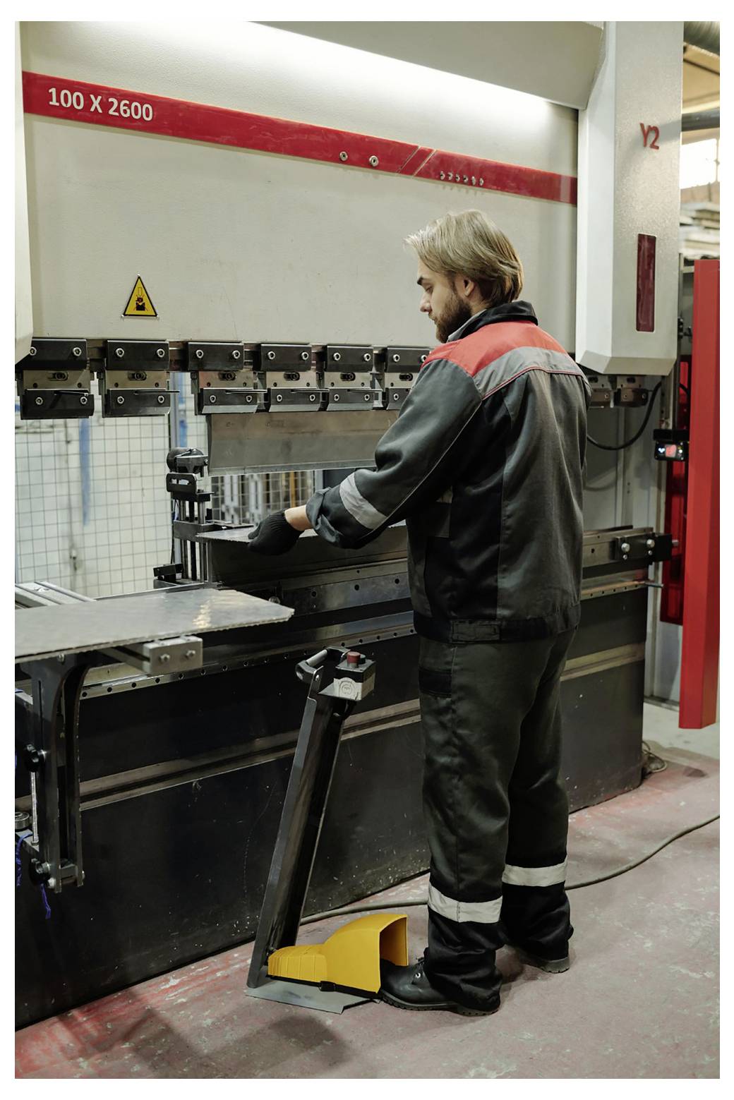 Ouvrier d'usine opérant une grande machine à plier industrielle, positionnant une tôle métallique pour le pliage dans un atelier.
