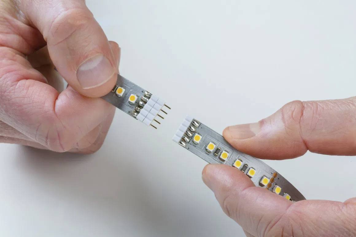 Deux mains tiennent chacune une extrémité d'une bande LED flexible qui est assemblée à un connecteur.