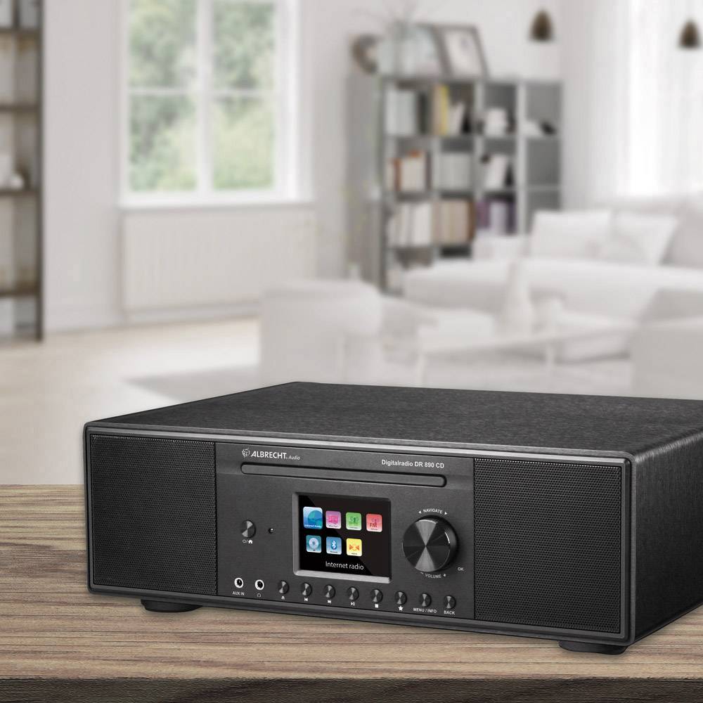 Un appareil de lecture audio noir est posé sur une table dans un salon moderne. À l'arrière-plan, on aperçoit des canapés blancs et une bibliothèque.