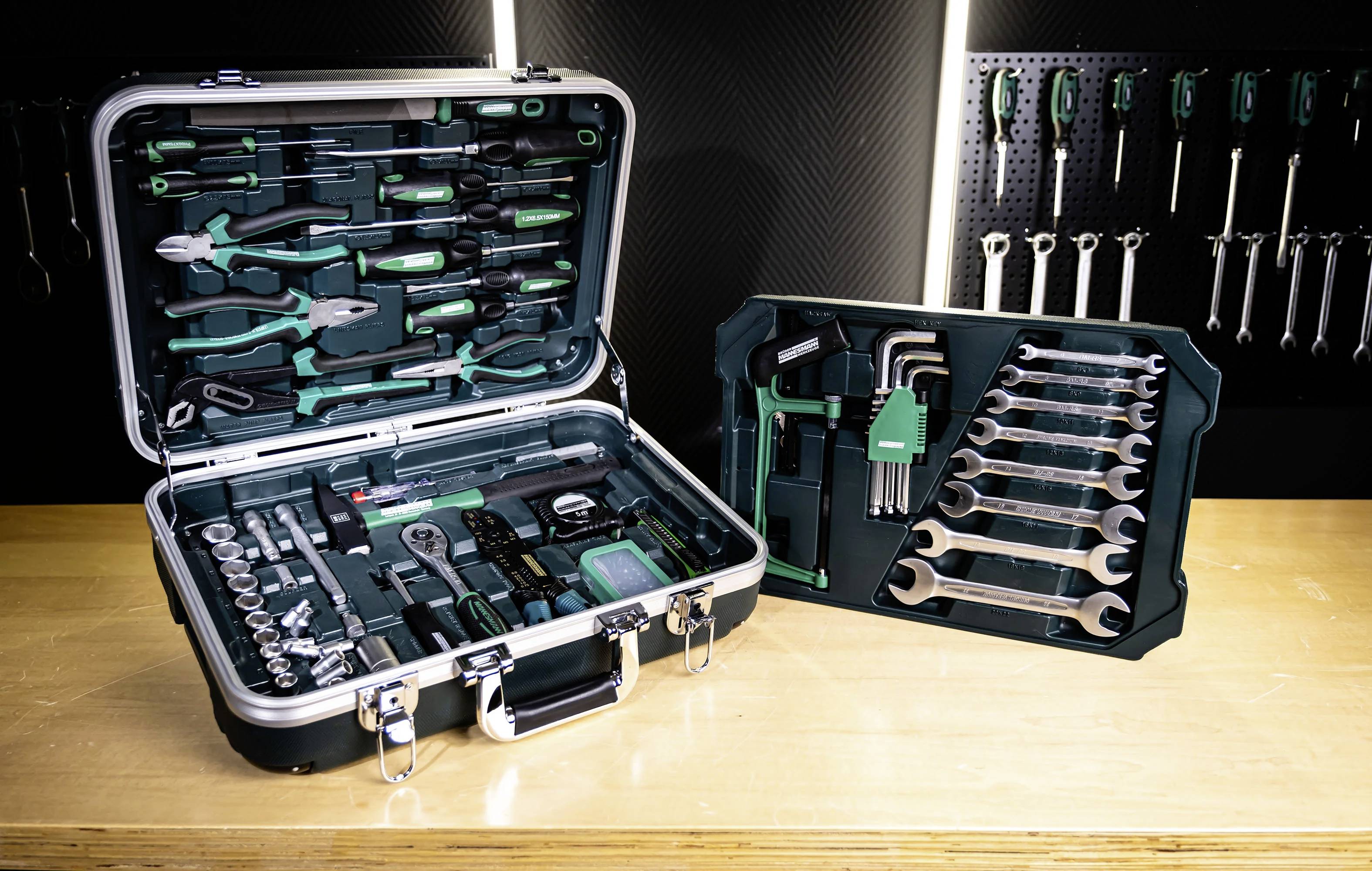 Des boîtes à outils contenant diverses clés, pinces, douilles et tournevis sont disposées sur un établi. Un panneau perforé supporte des outils supplémentaires.