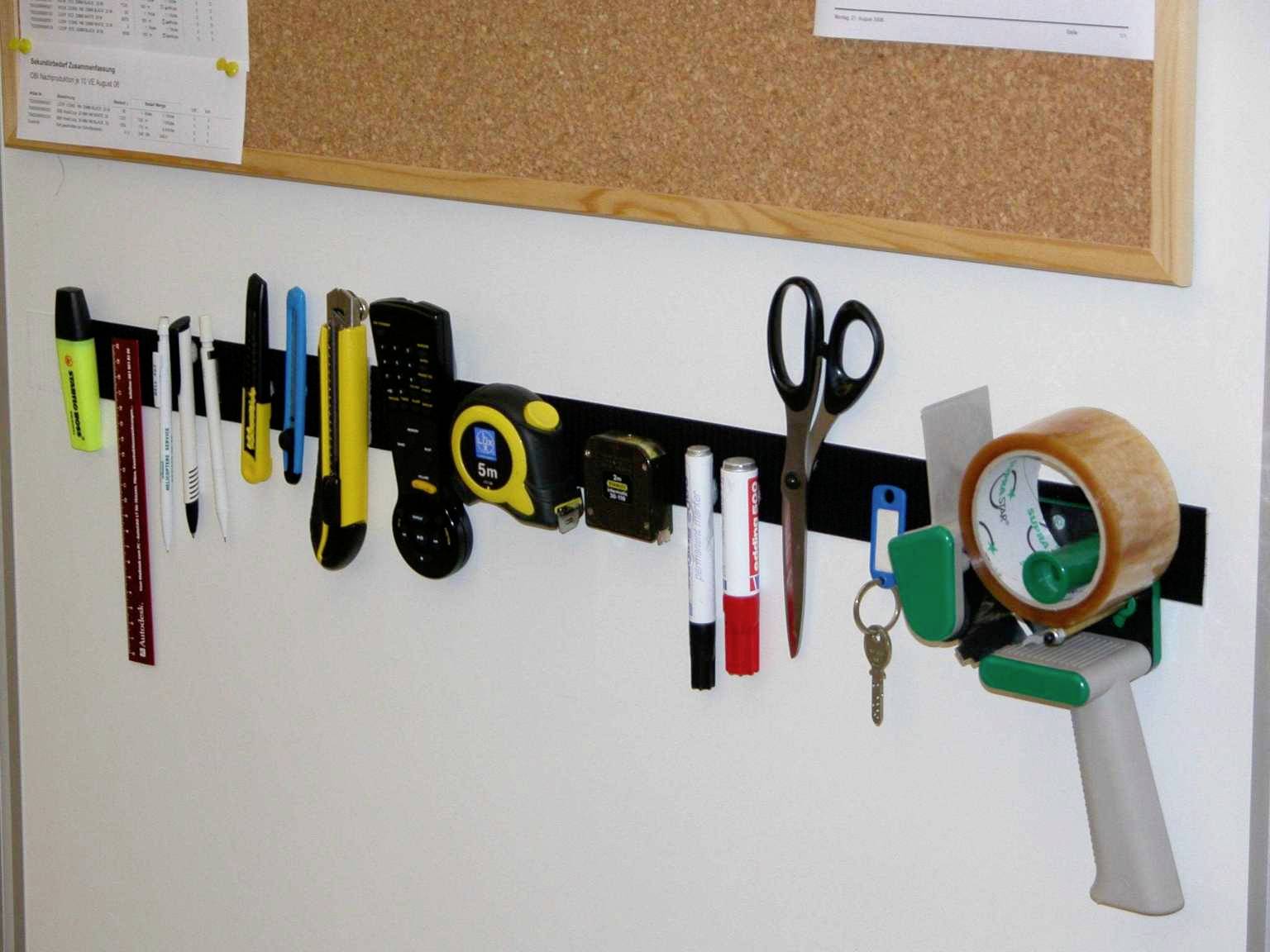 'Étagère murale avec divers outils de bureau et d'écriture tels que des stylos, des ciseaux et un distributeur de ruban adhésif devant un tableau d'affichage.'