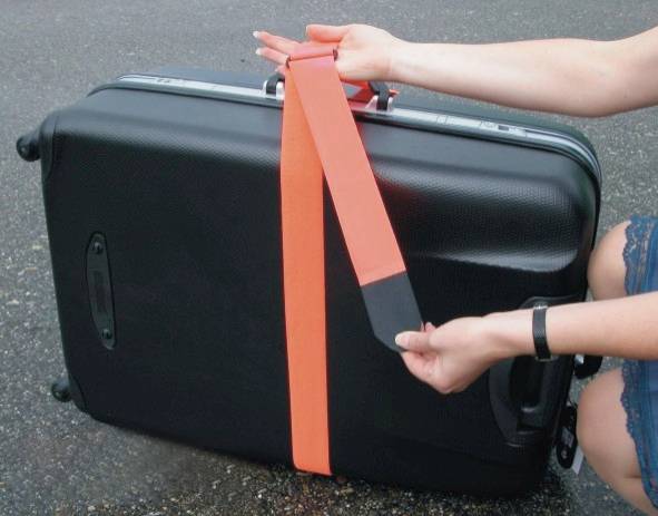 Une personne tient une sangle rouge vif, fixée à une valise noire sur l'asphalte. La sangle sert à stabiliser et à manipuler le bagage en toute sécurité.