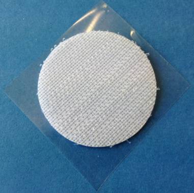 Un pansement textile rond et blanc sur une surface bleue, entouré de ruban adhésif transparent.