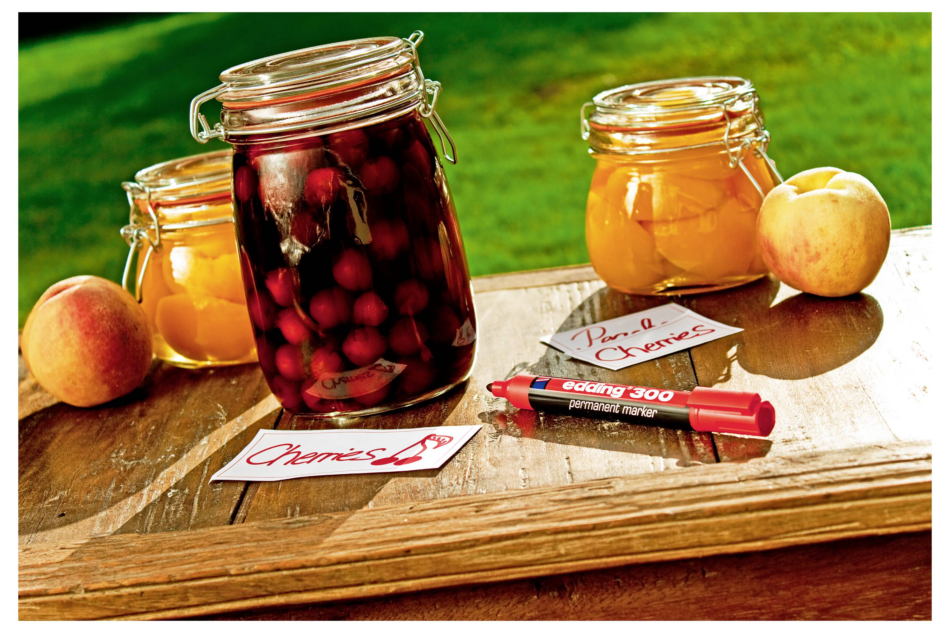 Pots de conserves maison sur une table en bois, incluant des conserves de cerises et d'abricots, avec des fruits frais et des étiquettes étiquetées.
