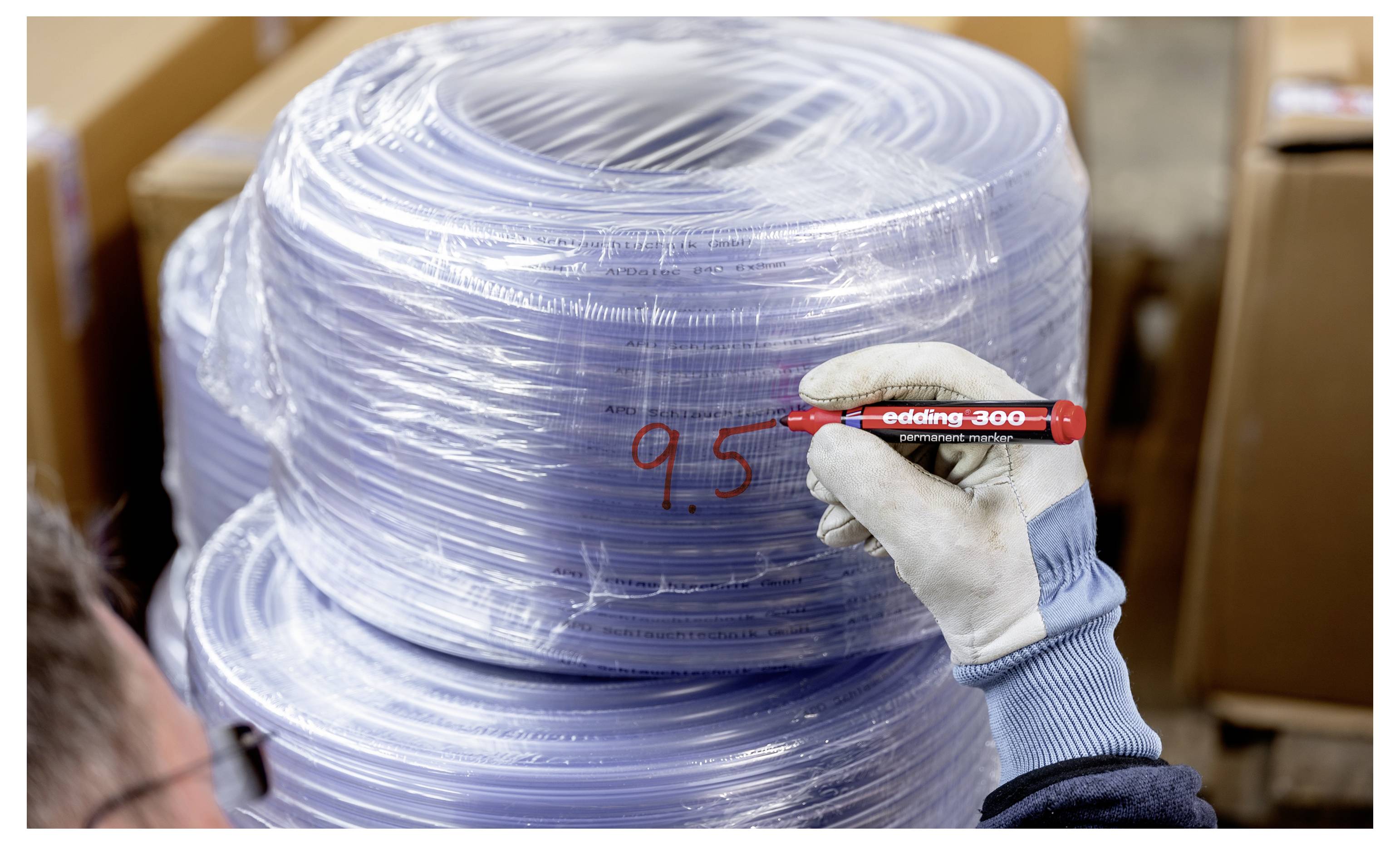 Travailleur ganté marquant « 9,5 » sur une grande bobine empilée enveloppée dans un plastique transparent, ce qui suggère une inspection d'inventaire ou un étiquetage.
