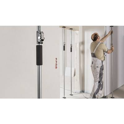 Un ouvrier installe un support sur un mur avec d'autres supports en arrière-plan. Il porte des vêtements de protection et s'agenouille.