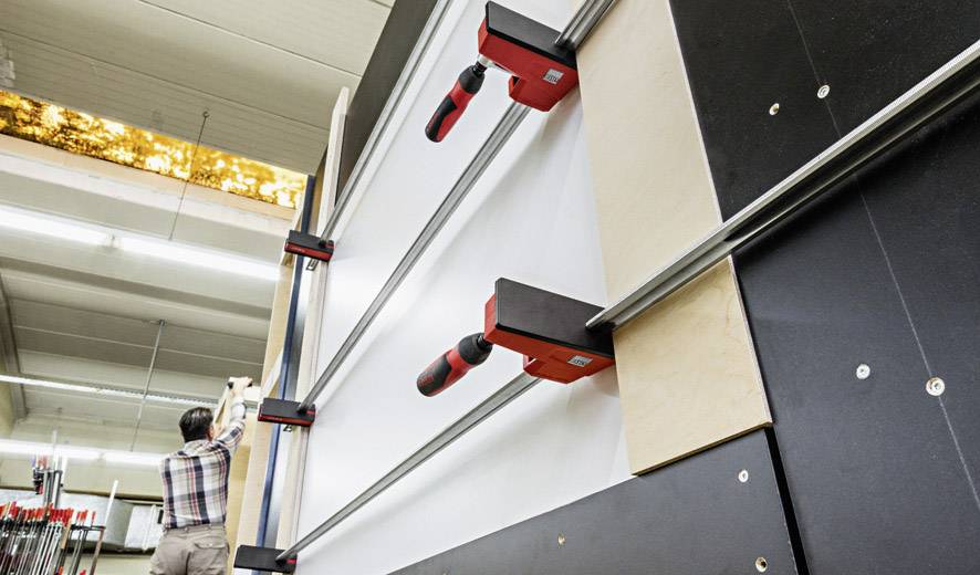 Une personne bloque une planche de bois dans une grande machine industrielle. L'installation est reconnaissable dans un environnement d'atelier.