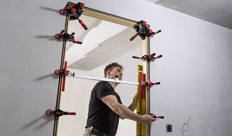 Un artisan ajuste un cadre de porte à l'aide de plusieurs serre-joints et d'un niveau à bulle pour garantir un positionnement précis.