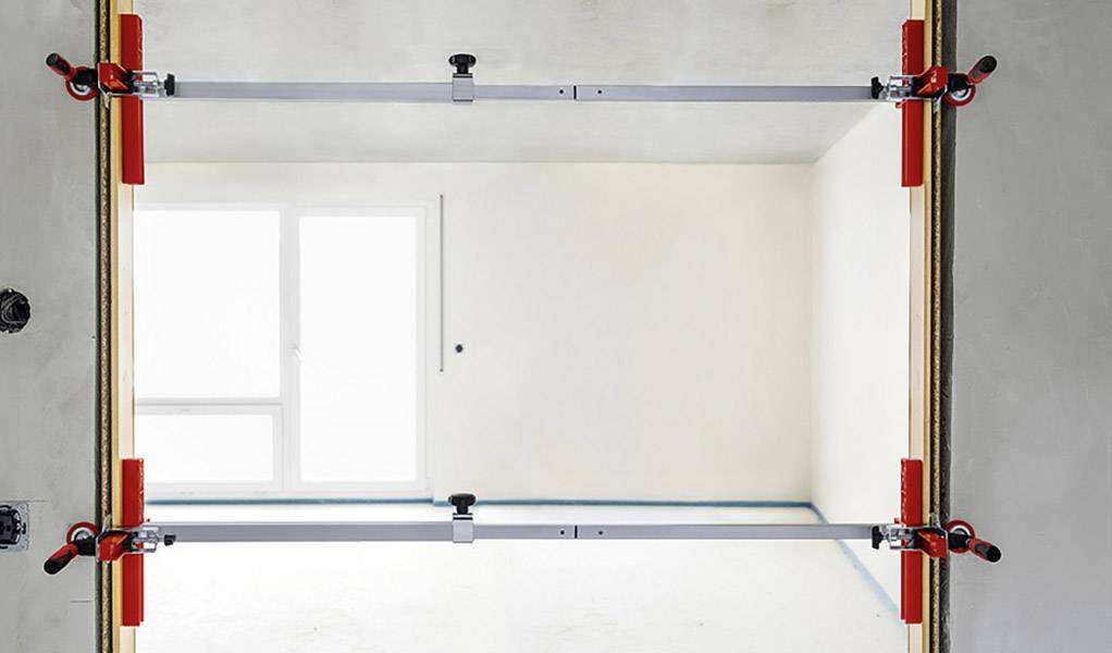 Encadrement de porte avec deux supports métalliques pour la stabilisation, sur un fond de pièce claire et vide avec une grande fenêtre.