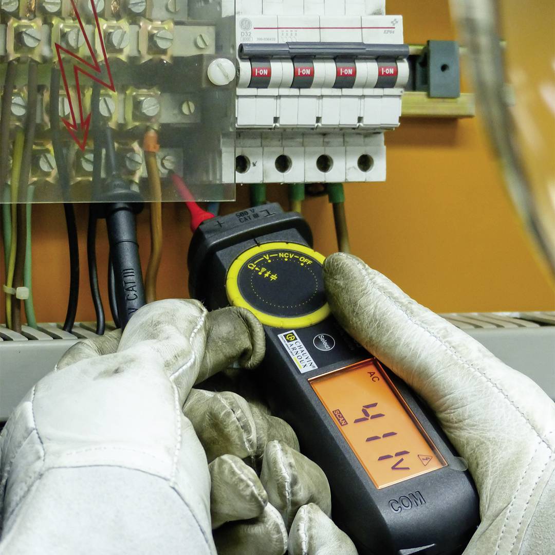 Une personne vérifie la tension électrique dans un armoire électrique à l'aide d'un multimètre ; tension affichée : 411 V.
