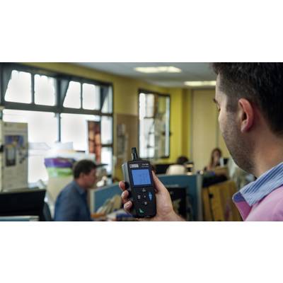 Un homme tient un appareil de mesure de la qualité de l'air dans un bureau, des personnes travaillent à des bureaux en arrière-plan.