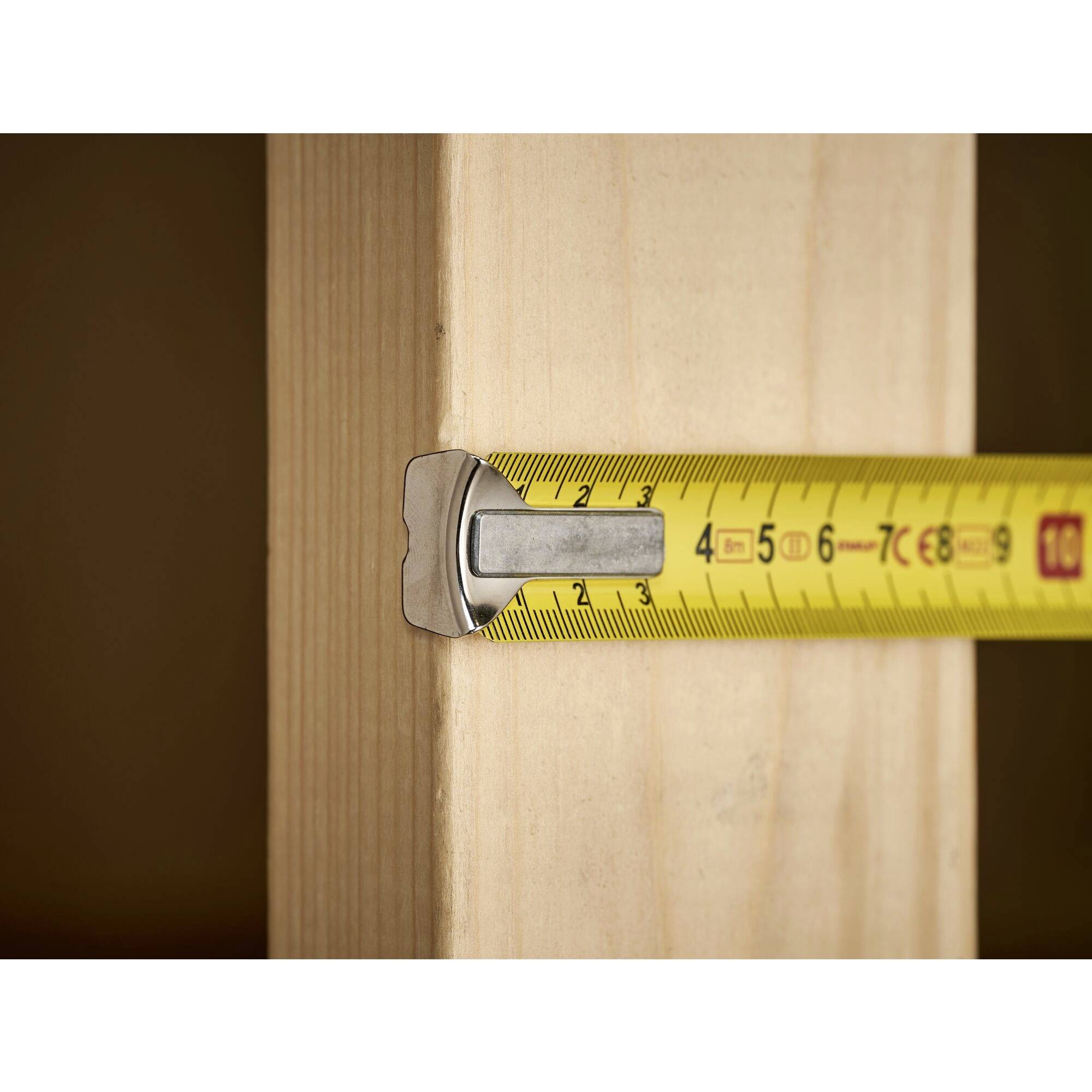 Un mètre ruban jaune mesure une planche en bois. Le mètre ruban indique environ 6,3 cm.