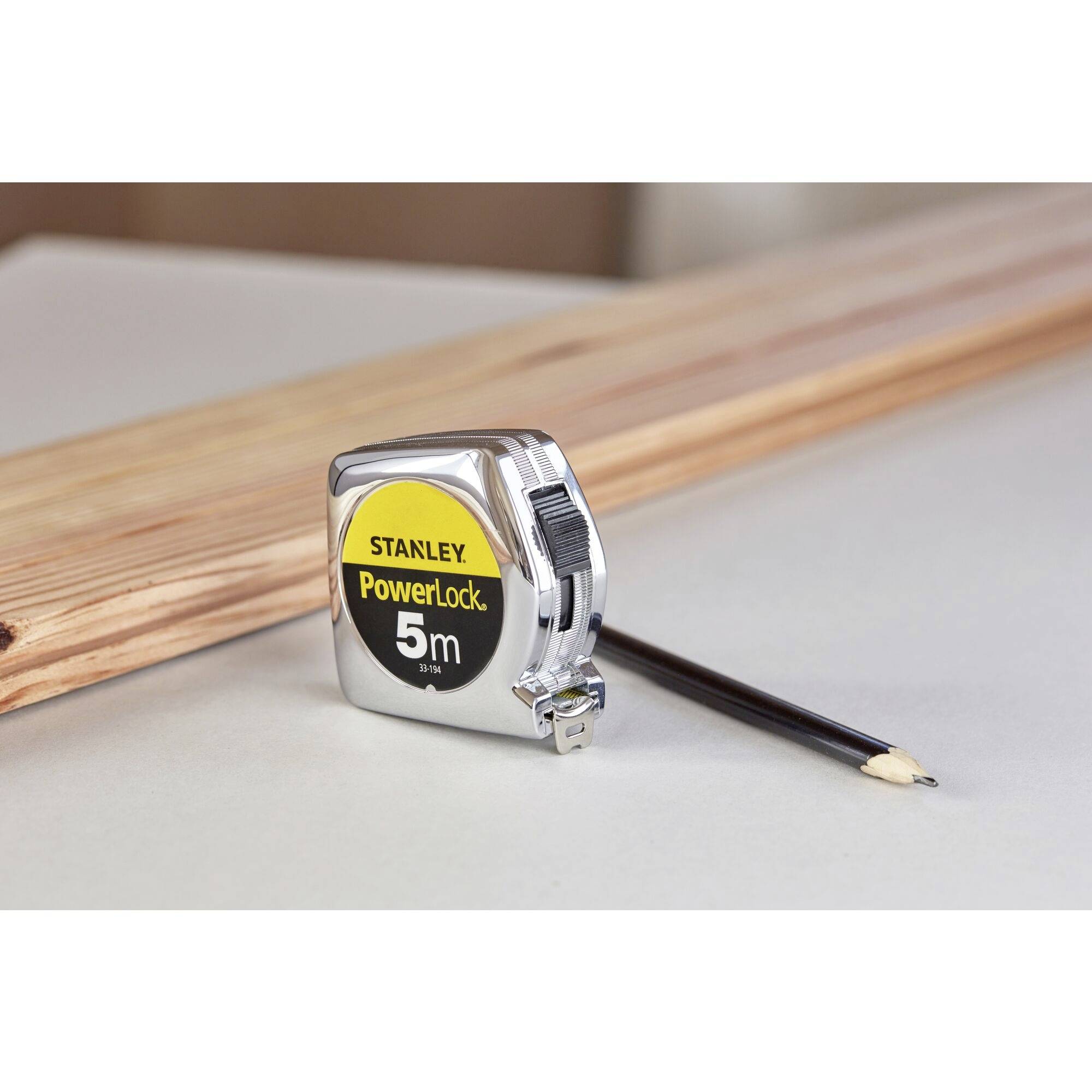 Un mètre ruban de 5 mètres et un crayon sont posés sur une poutre en bois, prêts pour des travaux de mesure ou de construction.