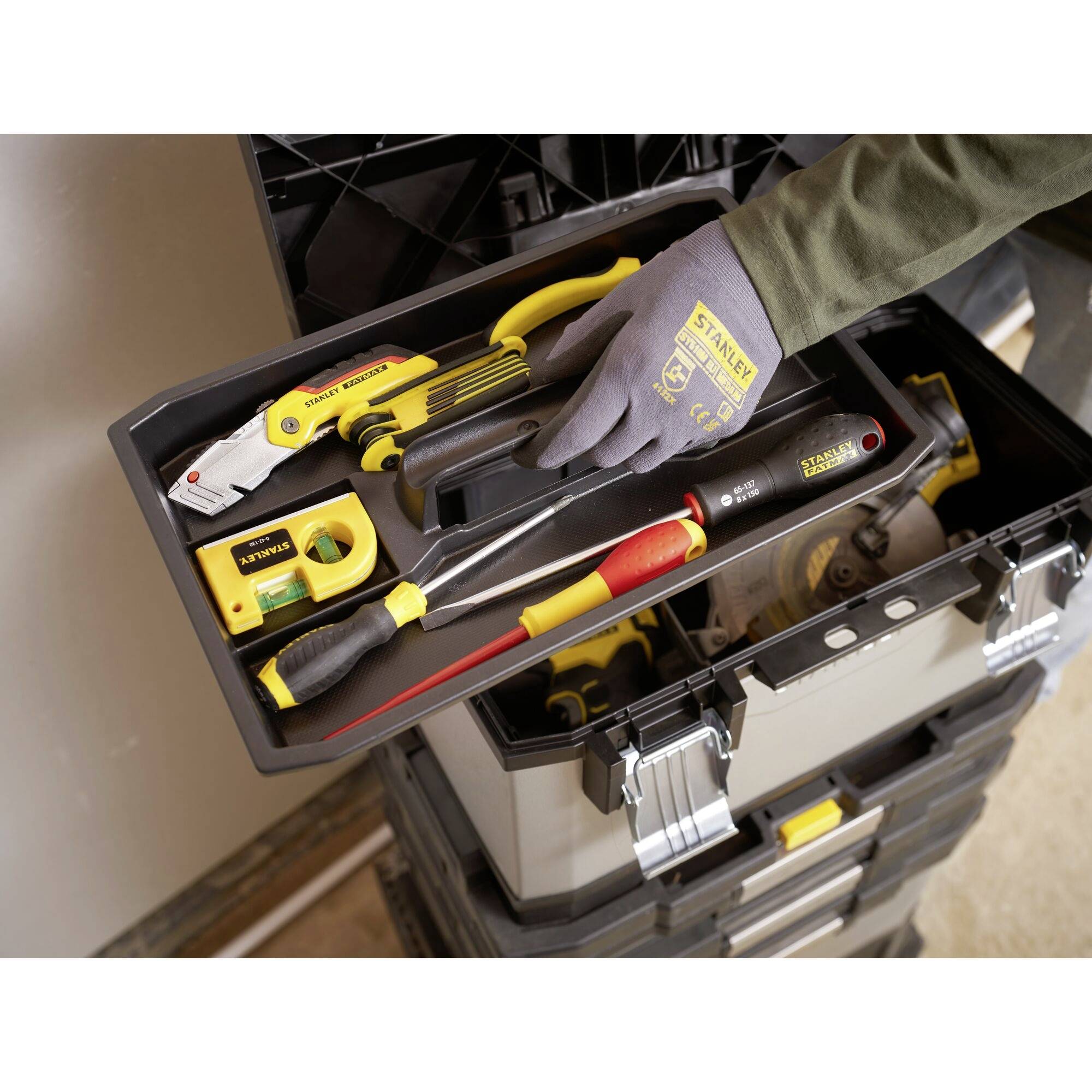 Une main tient une boîte à outils contenant divers outils manuels, dont un tournevis et un mètre ruban.