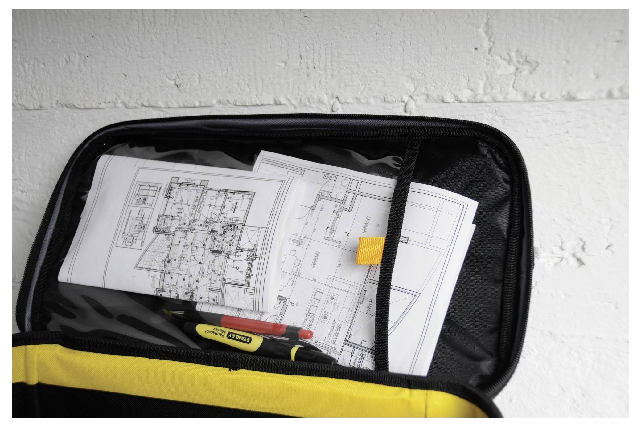 Un sac noir ouvert révèle des plans d'architecture et plusieurs stylos.