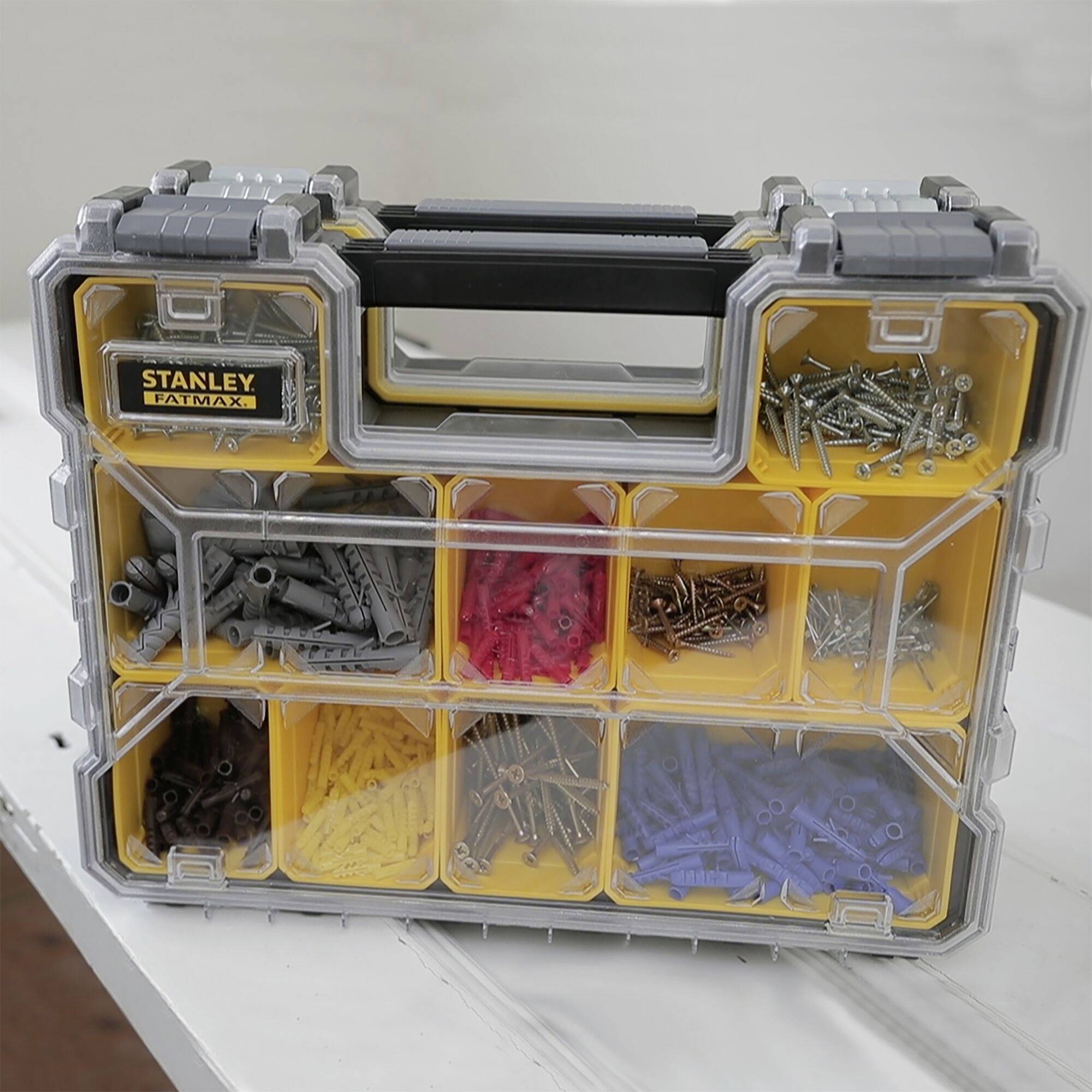 Une boîte à outils transparente à plusieurs compartiments, remplie de vis et de chevilles de différentes couleurs.