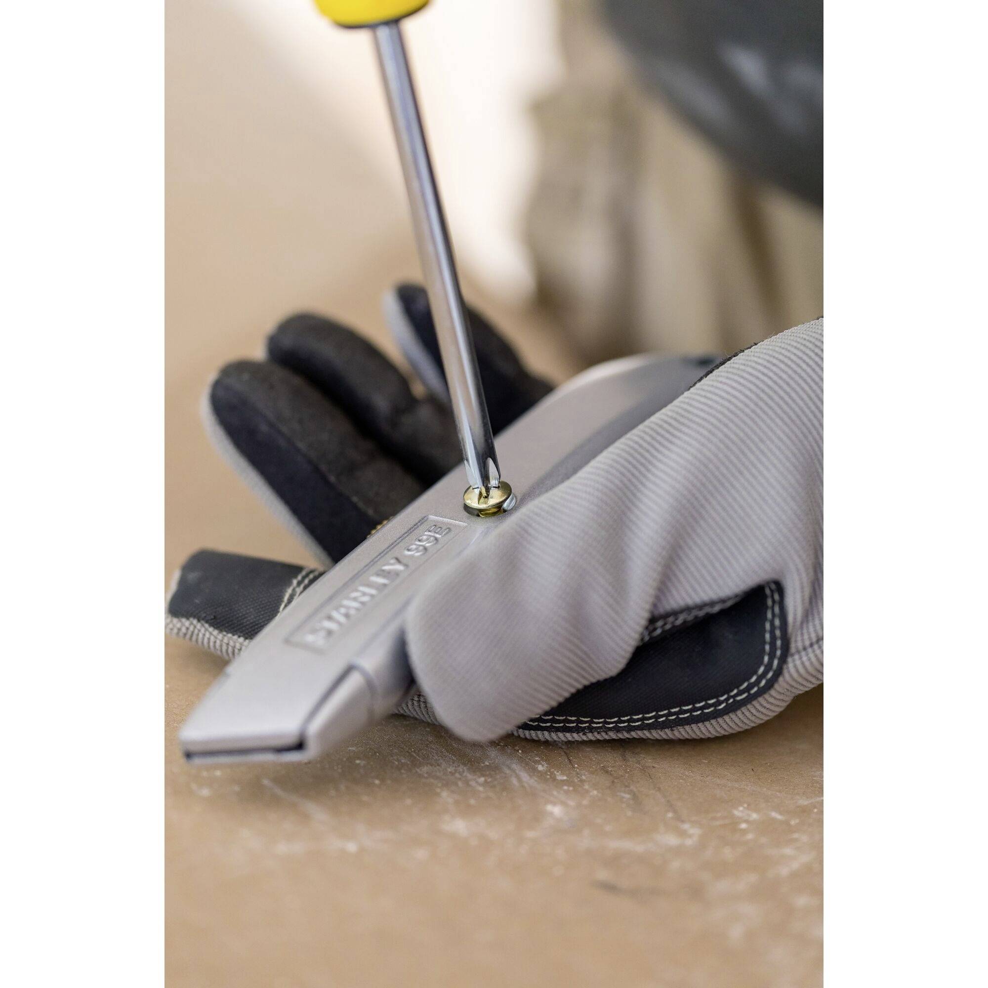 Une personne portant des gants tourne une vis dans un couteau pliant à l'aide d'un tournevis sur un fond en bois.